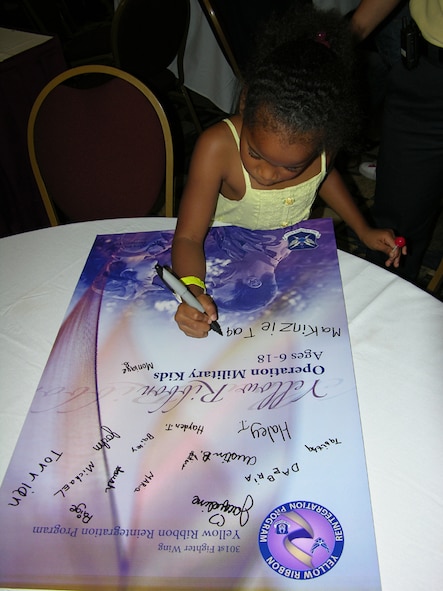 Makinzie Taplin, daughter of Staff Sgt Charles Taplin, a member of the 301st Fighter Wing's 73rd Aerial Port Squadron, joined her group in signing a commemorative poster to celebrate the 301st's inaugural Yellow Ribbon Reintegration Program. The event took place Saturday, July 25, at the Radisson Hotel Fort Worth - Fossil Creek. It featured a day of adult and child activities focussed on bringing families closer together and tackling military family-unique challenges in the midst of ongoing deployments worldwide. (U.S. Air Force Photo/MSgt Shawn David McCowan)