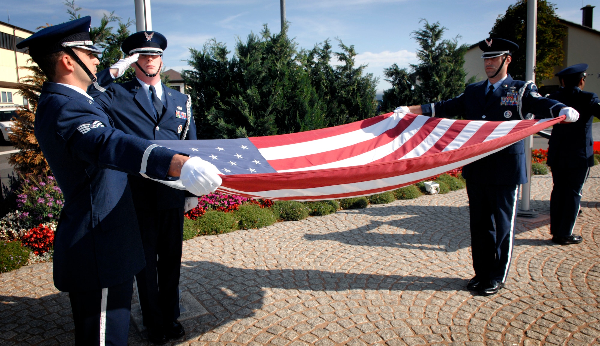 SPANGDAHLEM AIR BASE Germany – Honor Guardsmen Staff Sgt. Christopher Johnson and Tech. Sgt. Lee Haynor unfurl the American flag while Staff Sgt. Douglas Morrissey renders a salute during a Sept. 11 retreat ceremony honoring those who lost their lives during the attacks in 2001. Approximately 200 people from the 52nd Fighter Wing and tenant units attended the ceremony put together by the First IV.  (U.S. Air Force photo/Master Sgt. Bill Gomez)