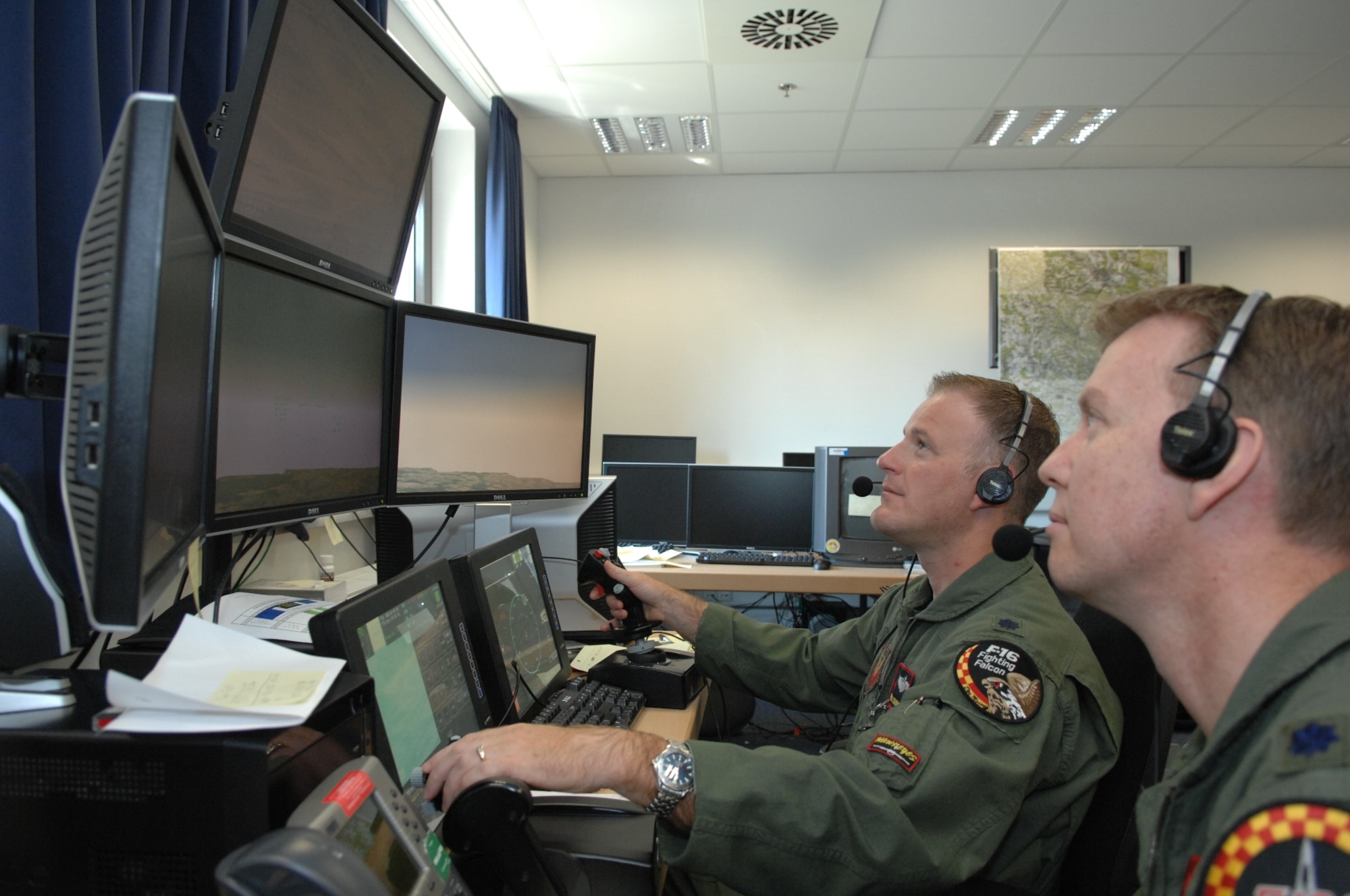 EINSEIDLERHOF AIR STATION, Germany-- Lt. Col. Travis Crawmer works the controls of an Advanced Tactical Aircraft Simulator, as Lt. Col Mike McMillan observes, at the U.S. Air Forces in Europe Warrior Preparation Center to enhance close air support training for joint terminal attack controllers and the U.S. Army during a Mission Readiness Exercise.   The two colonels, who recently returned from Southwest Asia deployments and are about to go back in the coming months, are F-16 fighter pilots from the Air National Guard’s 132nd Fighter Wing in Des Moines, Iowa sent temporary duty to USAFE to fly the live, virtual, constructive simulator since the WPC doesn’t have pilots that are current qualified in the cockpit. (U.S. Air Force photo/Master Sgt. Corey Clements)