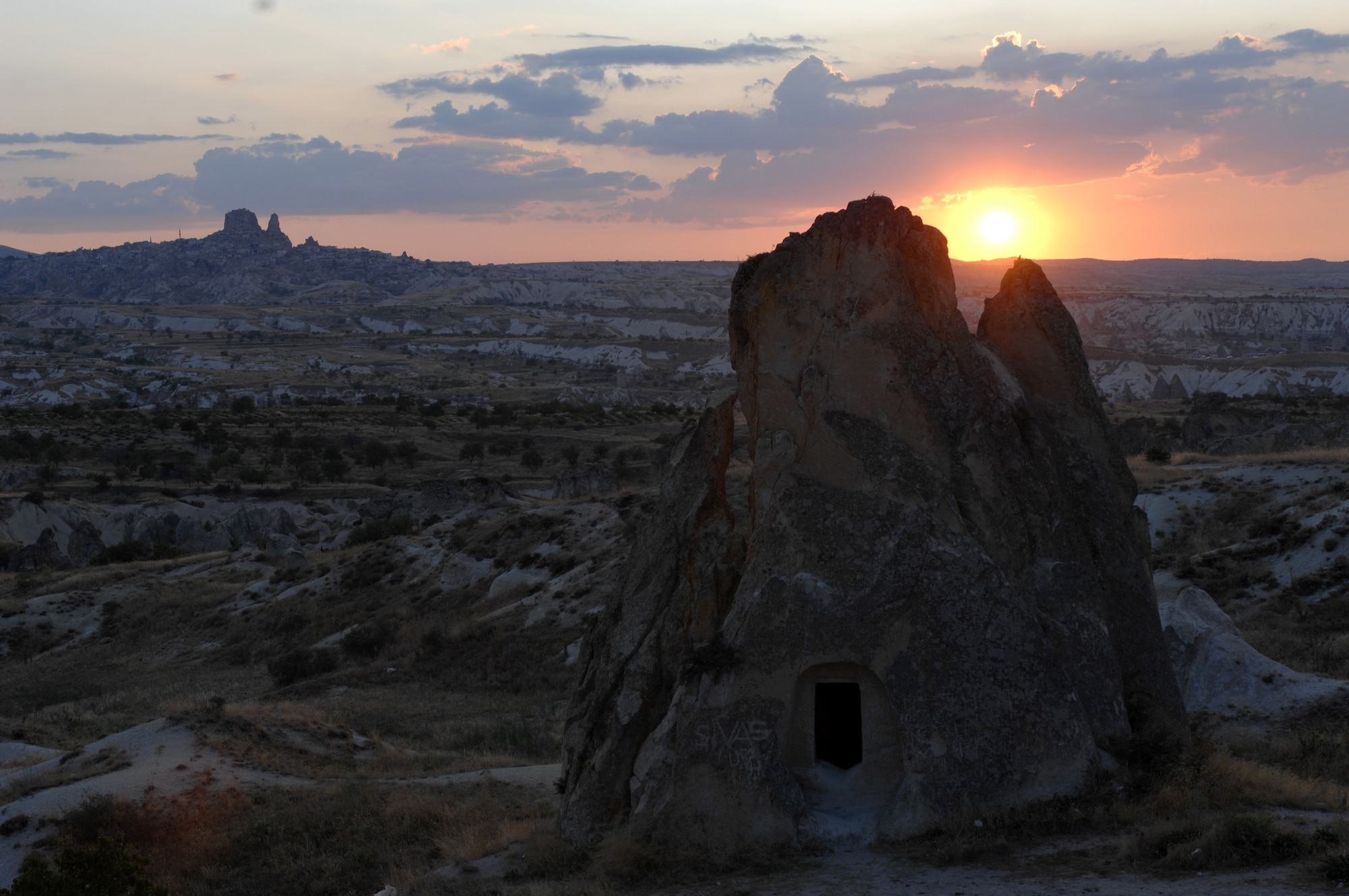 The sun sets behind a stone house which sits in front of the Ortahisar Castle in the region of Cappadocia, Turkey. Ortahisar translates to middle castle, which received its name from its central location to multiple towns within the region. Many settlements, from small cave houses to elaborate underground cities, have been excavated throughout the region. (U.S. Air Force photo/Staff Sgt. Lauren Padden)
