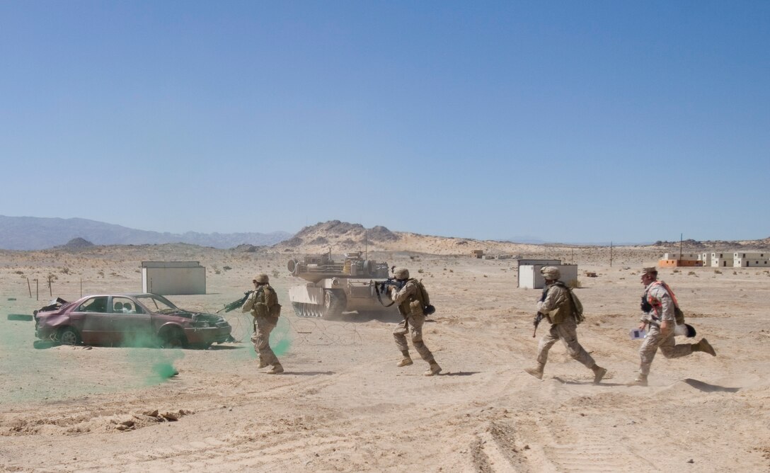 Lava Dogs from 1st Battalion, 3rd Marine Regiment, trailed closely by a TTECG “Coyote” evaluator, cross an open danger area under the cover of smoke and tanks during Bravo Company’s assault at Range 200 as part of their first phase of the Clear, Hold, Build Exercise during their training at the Enhanced Exercise Mojave Viper.