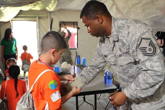 NELLIS AIR FORCE BASE Nev.,-- Anthony Vaiasuso Jr. simulates Self Aid and Buddy Care by wrapping a bandage around Master Sgt. Xavier King's right arm in the medical tent outside the Nellis youth center. SABC was being taught to the children during a mock deployment in support of the Kids Understanding of Deployment Operations program better known as Operation KUDO's.  Hundreds of military children participated in the Operation KUDO's deployment at the Nellis Air Force Base Sept. 12.
(U.S. Air Force photo by Tech. Sgt. Michael R. Holzworth)