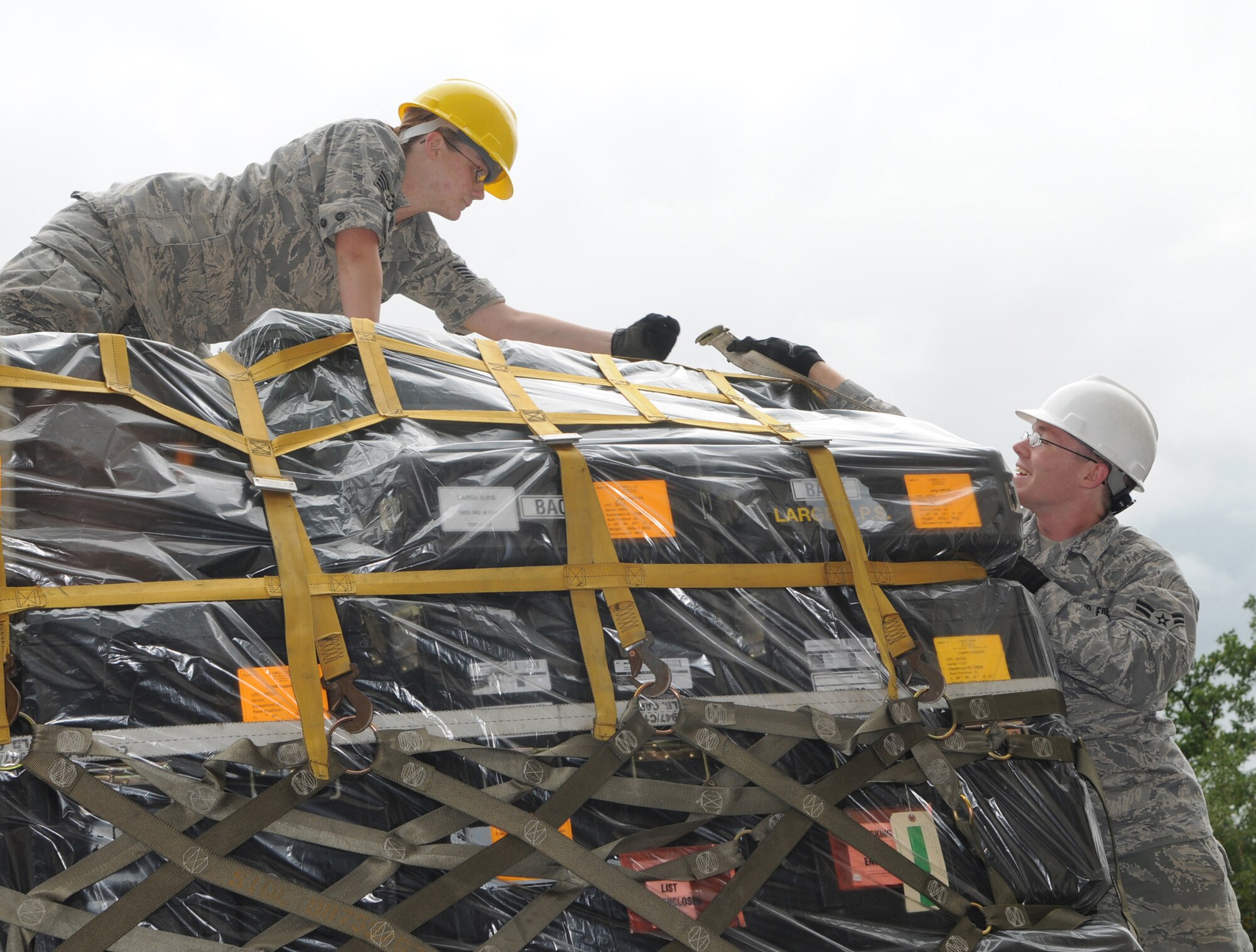 A1C Scott Morgan hands an end of a cargo strap to SSgt Katie Sawyer, members of the 1st Combat Communications Squadron, while securing a pallet in preparation for a convoy exercise from Ramstein Air Base Germany to Aviano Air Base Italy.  The convoy consists of seven trucks carrying approximately 10 tons of equipment. (U.S. Air Force photo by Tech Sgt. Sean Mateo White)