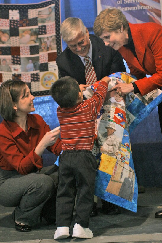 Sue Mullen, wife of Chairman of the Joint Chiefs of Staff Adm. Mike Mullen, joins Mike Landers, deputy national director of the Armed Forces YMCA in presenting an Operation Kid Comfort quilt to Nathan Jung and his mother, Cathy Jung. Quilts feature family photos and are delivered to the families of deployed service members about three months into a deployment. (U.S. Air Force photo/Master Sgt. Paul Dean)