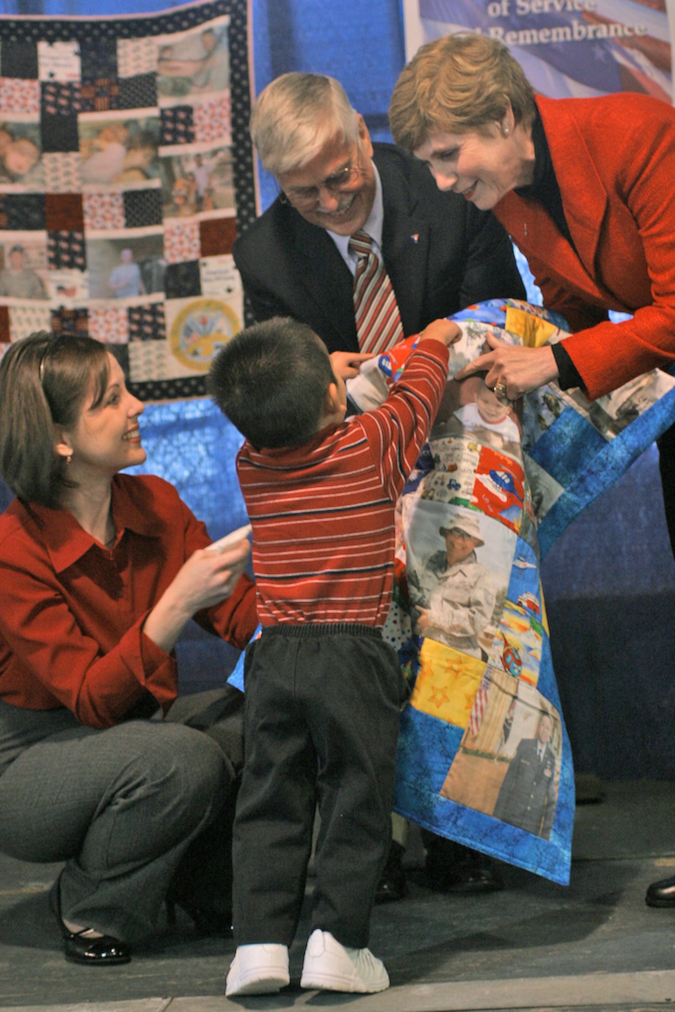 Sue Mullen, wife of Chairman of the Joint Chiefs of Staff Adm. Mike Mullen, joins Mike Landers, deputy national director of the Armed Forces YMCA in presenting an Operation Kid Comfort quilt to Nathan Jung and his mother, Cathy Jung. Quilts feature family photos and are delivered to the families of deployed service members about three months into a deployment. (U.S. Air Force photo/Master Sgt. Paul Dean)