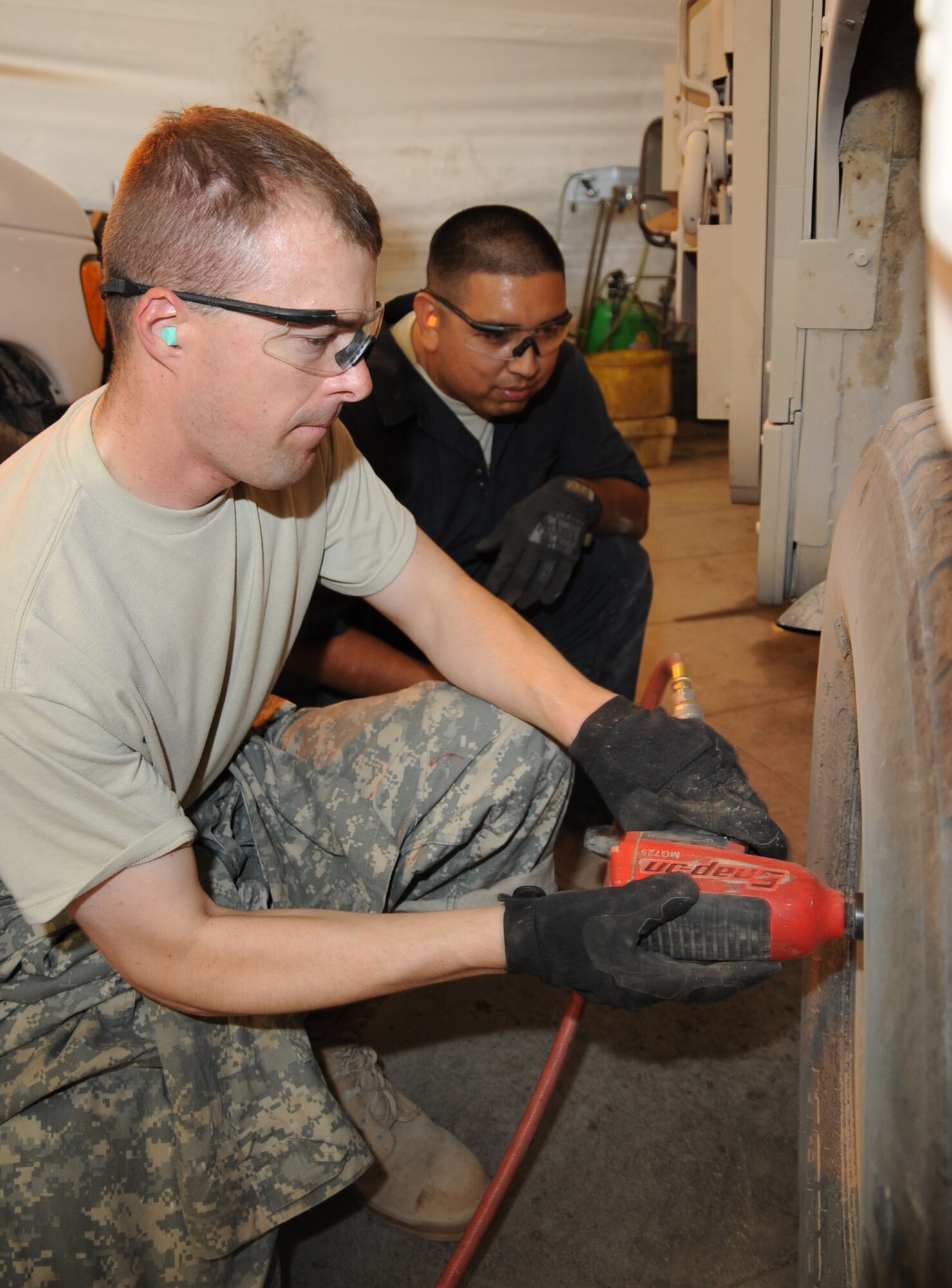 SATHER AIR BASE, Iraq -- Staff Sgt. Paul Porras (right), 447th Expeditionary Logistics Readiness Squadron vehicle equipment journeyman, observes Chaplain (Capt.) Chad Montgomery, 447th Air Expeditionary Group, using an air power tool to remove a tire from a Humvee here Sept. 11, 2009.  Chaplain Montgomery has made it his goal to get involved by helping Airmen with their daily missions and training during his deployment. Sergeant Porras is deployed from Keesler Air Force Base, Miss., and is a native of San Antonio, Texas. Chaplain Montgomery is deployed from Lackland AFB, Texas and is a native of Newtown Square, Pa. (U.S. Air Force photo/Tech. Sgt. Johnny L. Saldivar/Released)