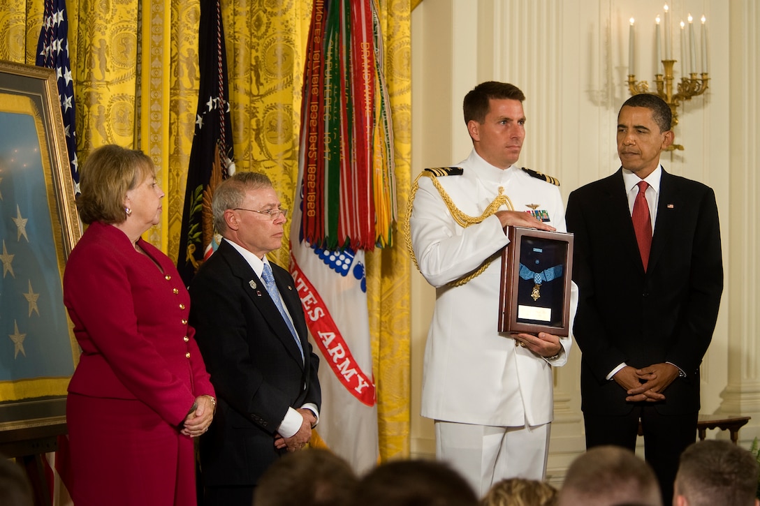 A Navy lieutenant commander holds the Medal of Honor that President Barack Obama posthumously awarded to Army Sgt. 1st. Class Jared C. Monti, as his parents, Paul and Janet Monti, from Raynham, Mass., stand by in the East Room of the White House in Washington D.C., Sept. 17, 2009. "Jared Monti saw danger before him and he went out to meet it," Obama said in the ceremony.  U.S. Army photo by D. Myles Cullen