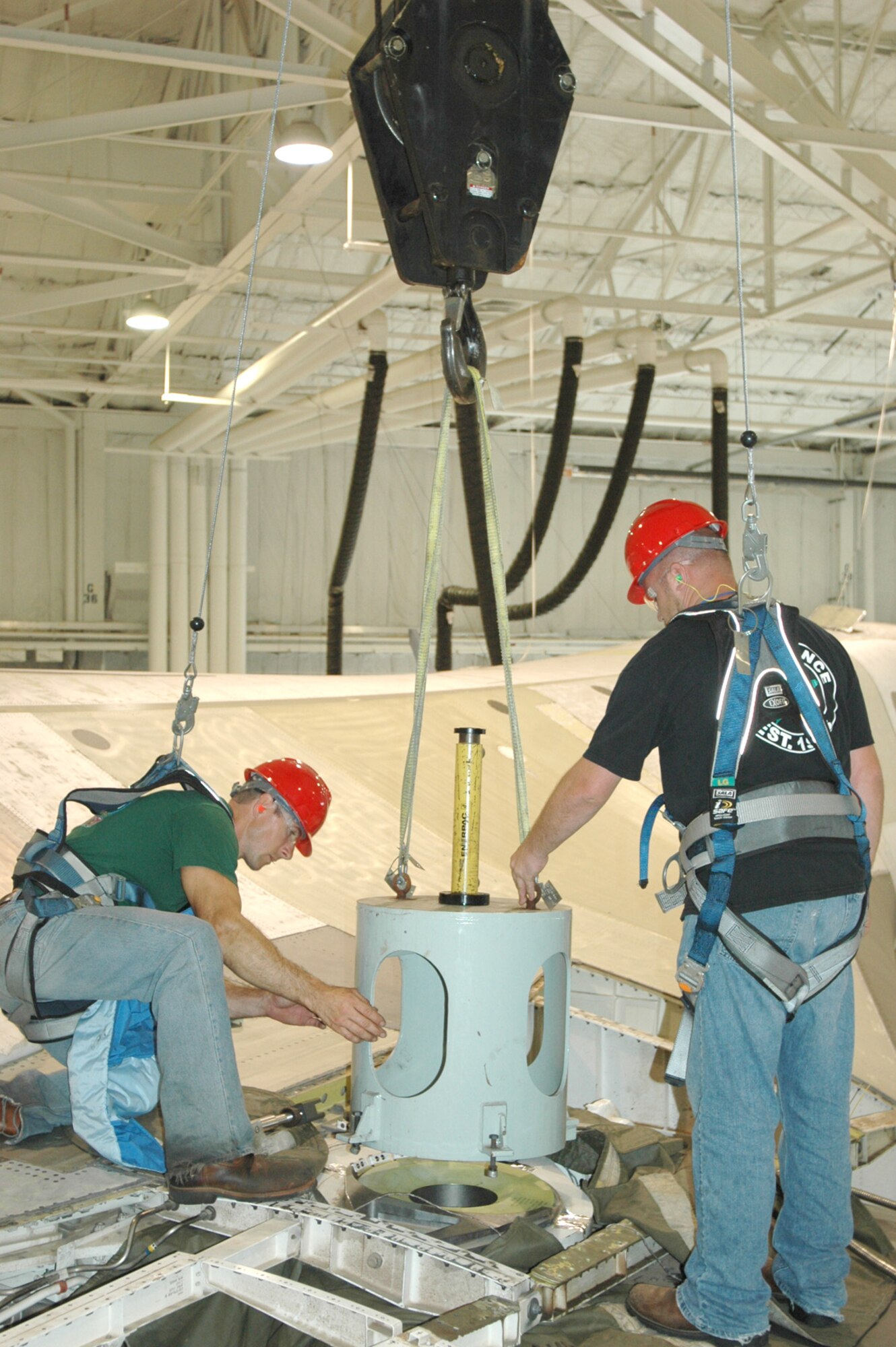Workers place a bell housing over the pivot pin. The housing will be bolted to the area around the pin. The housing provides leverage for a hydraulic jack to force the pin out. (Air Force photo by Howdy Stout)
