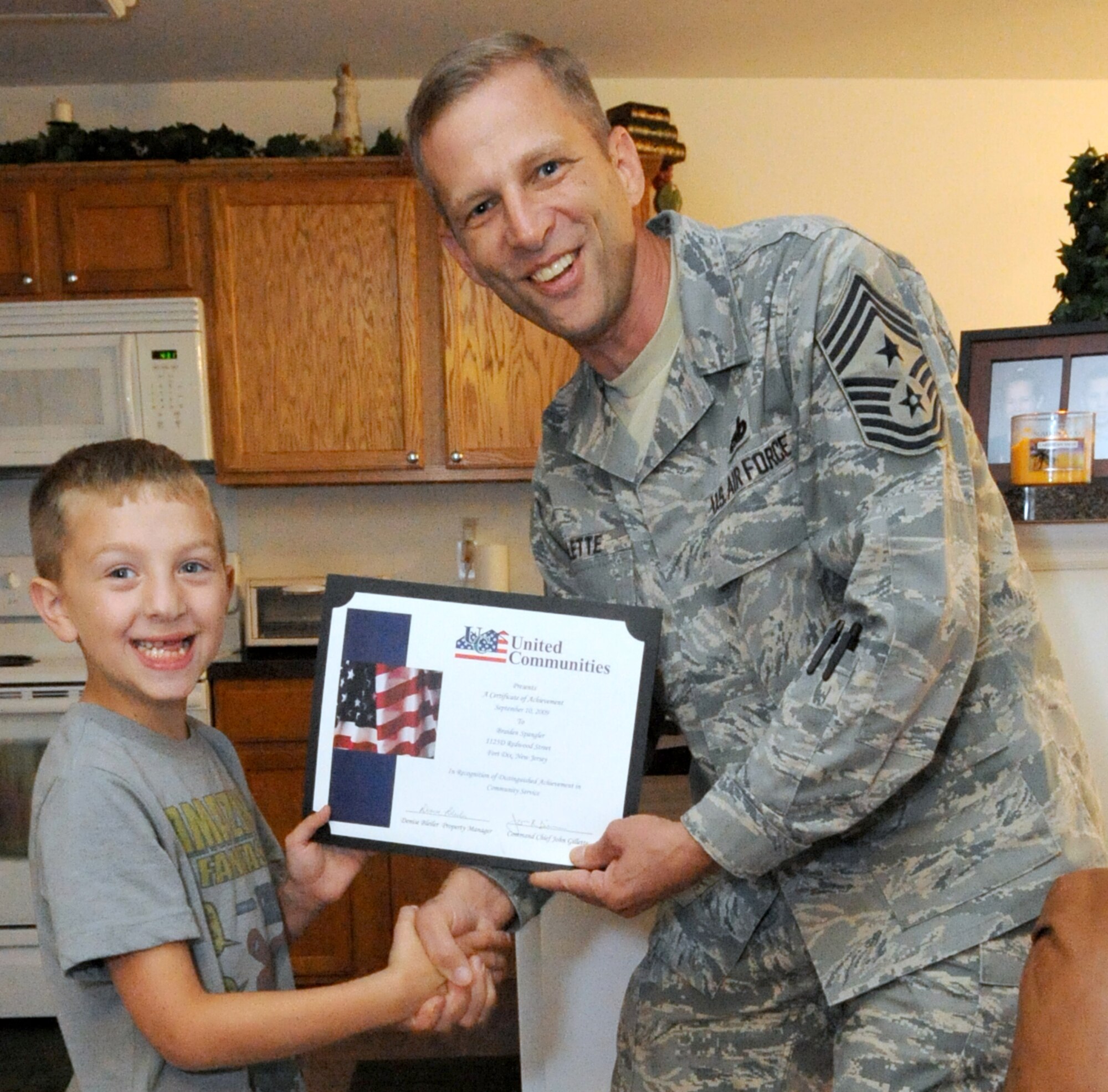 Braiden Spangler, 7, son of Special Agent Christopher Spangler, Office of Special Investigations Det 1, is honored by Chief Master Sgt. John Gillette, 305th Air Mobility Wing command chief, on behalf of United Communities here recently. Braiden responded to a request from UC asking for donations for children in schools and orphanages in Djibouti, Africa. Braiden broke his piggy bank to give all he had and two large bags of his own clothes to help others in need. UC will continue to accept donations to be sent to the children. (U.S. Air Force photo/Wayne Russell)