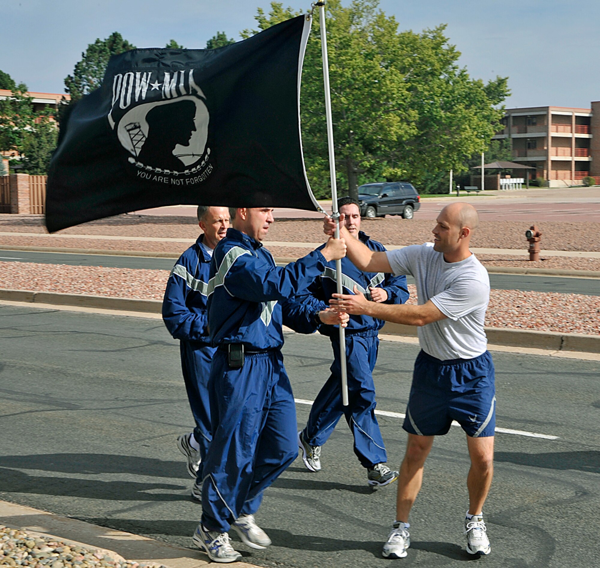 PETERSON AIR FORCE BASE, Colo. -- Col. Stephen Whiting, 21st Space Wing commander, passes the POW/MIA flag to Master Sgt. Lance Thibault, 50th Space Wing, completing the first leg of the 24-hour POW/MIA run Sept. 17.  Chief Master Sgt. Tim Omdal, 21st SW command chief, and Capt. Paul Scheglov, 21st SW executive officer, accompanied Colonel Whiting on the first leg of the run. The wing hosted several events during the week, including a reveille ceremony, the run and a candlelight vigil. The week culminated with a remembrance ceremony Sept. 18 at the base chapel, where retired Col. Gordon Scott, a former POW, was the guest speaker. (Air Force photo by Dennis Howk)