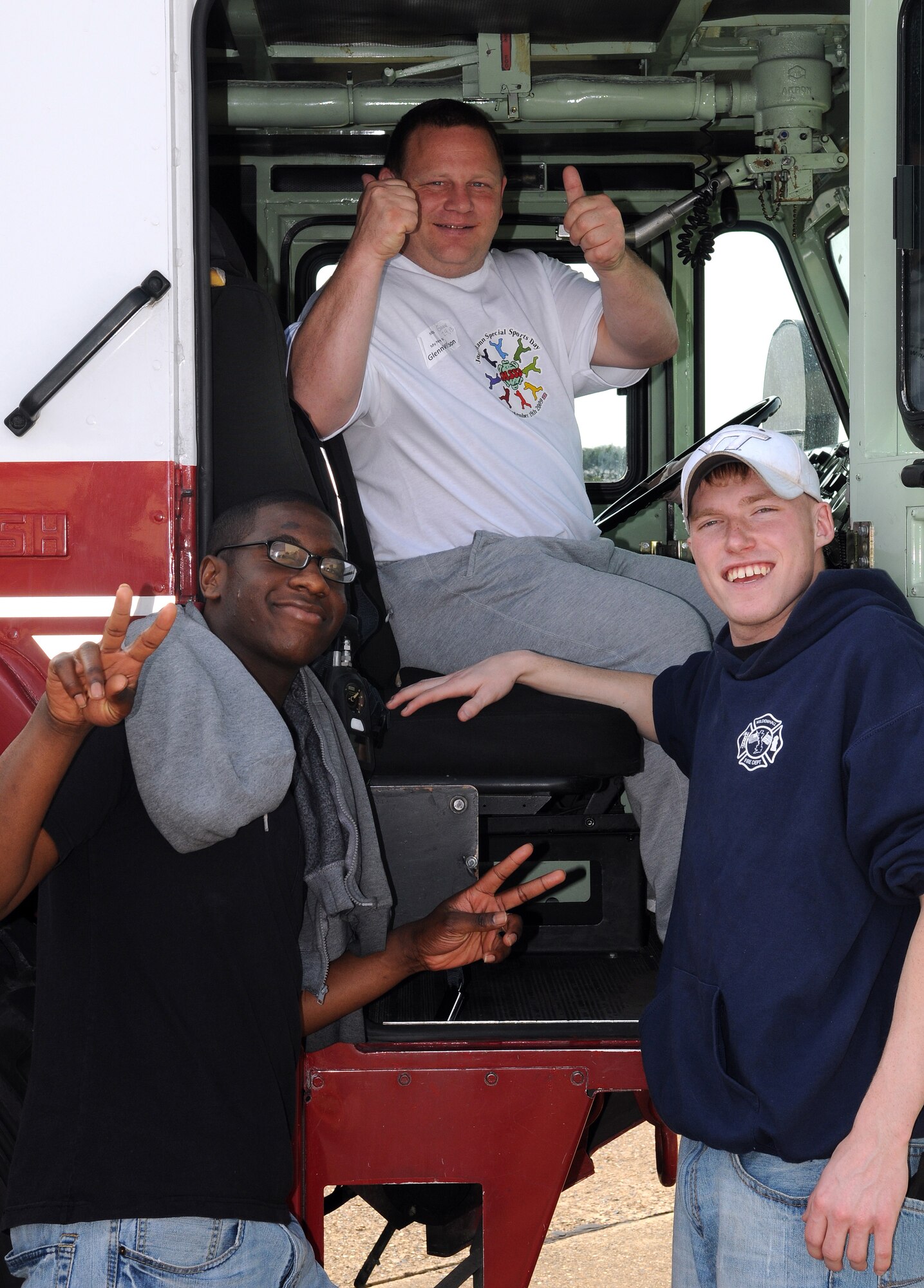 RAF MILDENHALL, England -- A Joan Mann Special Sports Day participant (middle) and his two escorts pose for a photo in a base fire truck at Hangar 711 Sept. 19. The sports day was designed to allow special-needs athletes to compete in a fun atmosphere. This was the 28th year RAF Mildenhall has hosted the event. (U.S. Air Force photo/Senior Airman Thomas Trower)