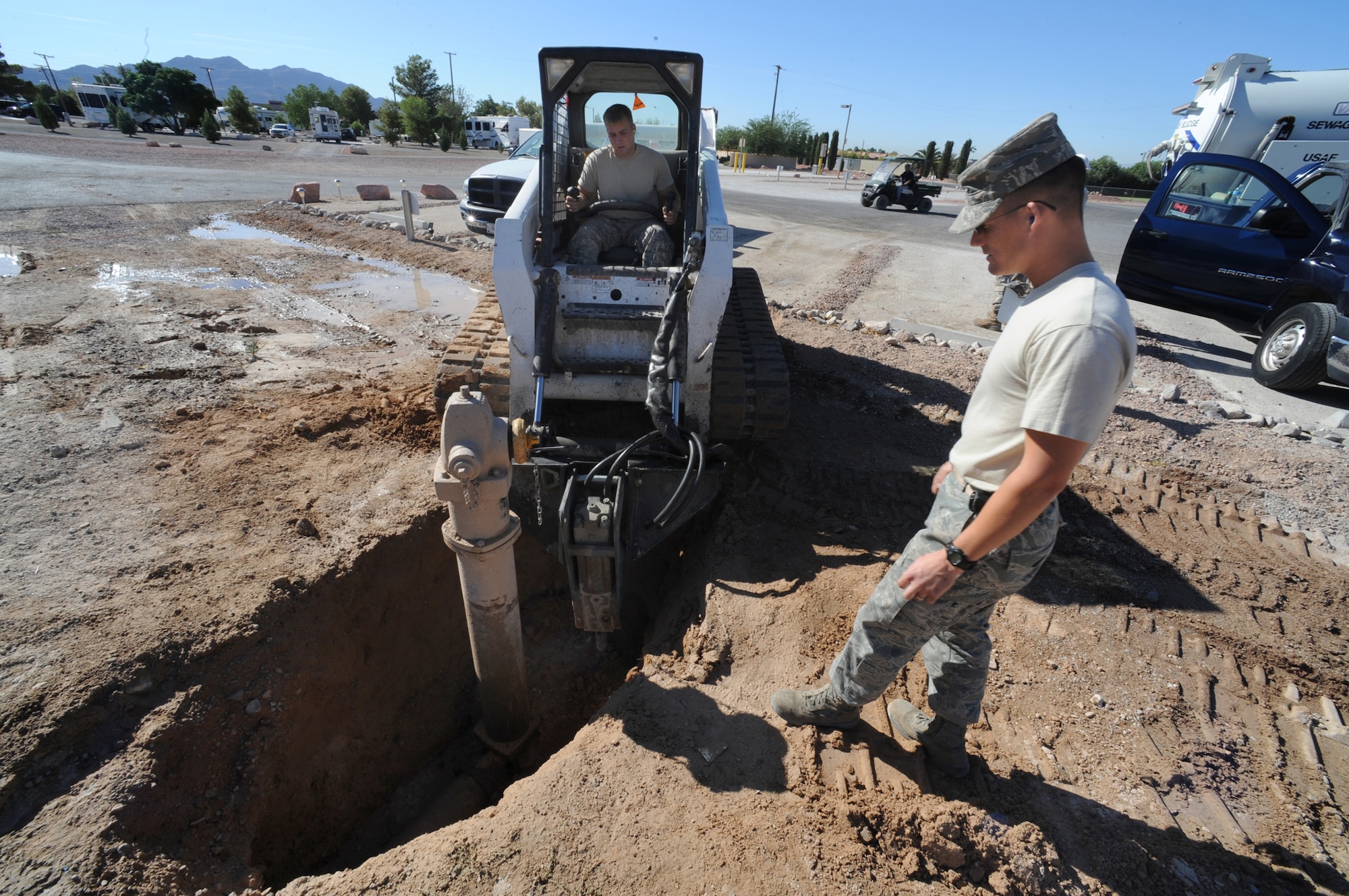 NELLIS AIR FORCE BASE, Nev. -- Tech. Sgt. Martin Spann directs Airman 1st Class Joseph Soper where to use a bobcat with a hydraulic jackhammer to break up a concrete "kicker" that keeps the main water line from bursting out the back of a fire hydrant in the  family campground, Sept. 23. Sergeant Spann and Airman Soper are 99th Civil Engineer Squadron pavements and construction operators helping replace 12 antiquated fire hydrants throughout the Nellis family campground.  
(U.S. Air Force photo by Tech Sgt. Michael R. Holzworth)
