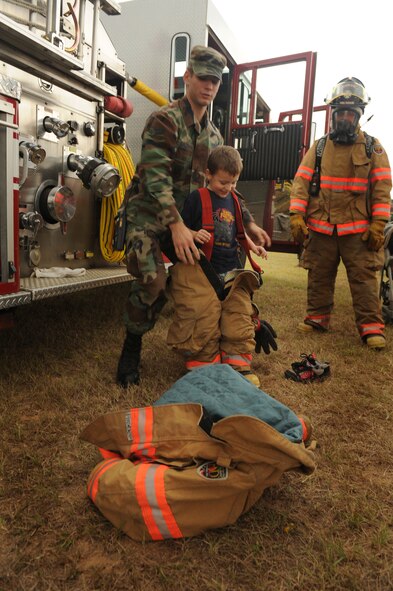 SHAW AIR FORCE BASE, S.C. -- Airman 1st Class Justin Salzman, 20th Civil Engineer Squadron Fire Department, helps Trystan Gray, age four, son of Staff Sgt. Richard Gray 20th Logistics Readiness Squadron, into a fire suit during "Operation Take-Flight", which is a simulated deployment to the fictional country Shawkikistan Sept. 17. Children, ages 4 through 12, got to experience what mom and dad go through when deploying which gives them a better understanding of the deployment process and helps relieve anxiety. (U.S. Air Force photo/Senior Airman David Minor)