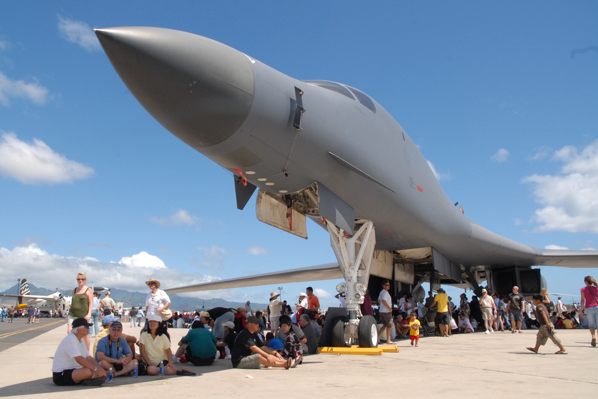 HICKAM AIR FORCE BASE, Hawaii -- Spectators to the ?Wings over the Pacific? Open House enjoy the shade of the B-1 Lancer, nicknamed the Bone, from Ellsworth Air Force Base, S.D., awaiting the Thunderbird aerial demonstration Sept. 19. The Thunderbirds, U.S. Air Force Demonstration Squadron, were the headliners during the open house. They demonstrate the capabilities the F-16 Fighting Falcon by performing combat maneuvers during their aerial demonstration. This is Hickam's first open house since 2003, and a crowd of nearly 100,000 paid a visit during the weekend. (U.S. Air Force photo/Staff Sgt. Mike Meares)