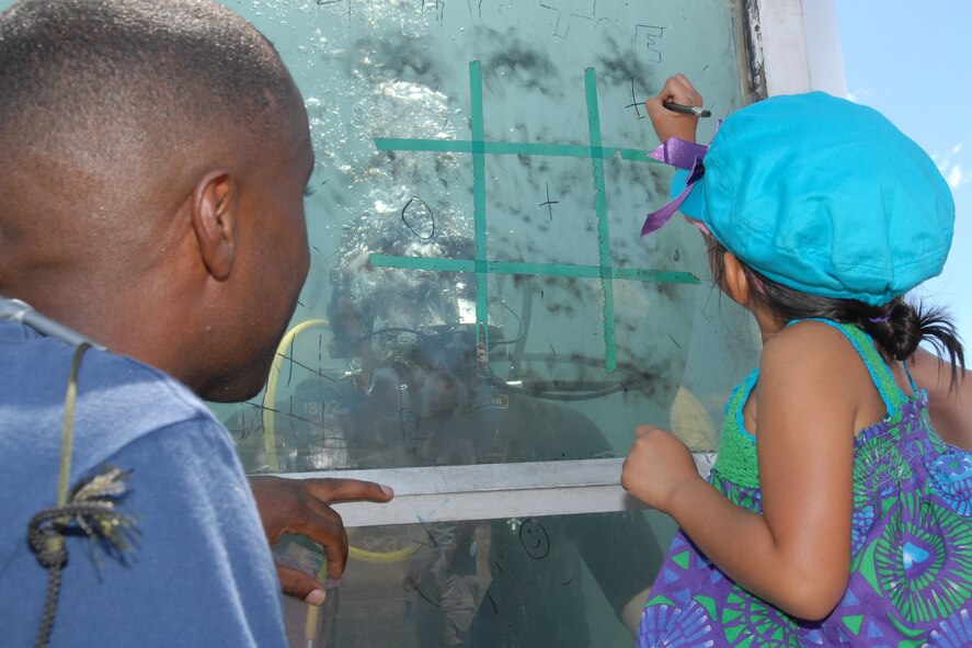 HICKAM AIR FORCE BASE, Hawaii -- Lorayne Aguinaldo, 4 years old, makes her mark on the glass of the dive tank while playing tic-tac-toe against Navy Diver 1 Mariano Zorde, Mobile Diving and Salvage Unit 1 Company 18, Pearl Harbor, Hawaii, during the Open House ?Wings Over the Pacific? weekend. The Thunderbirds, U.S. Air Force Demonstration Squadron, were the headliners during the open house. They demonstrate the capabilities the F-16 Fighting Falcon by performing combat maneuvers during their aerial demonstration. This is Hickam's first open house since 2003, and a crowd of nearly 100,000 paid a visit during the weekend. (U.S. Air Force photo/Staff Sgt. Mike Meares)