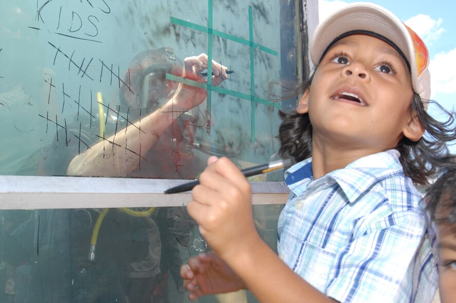 HICKAM AIR FORCE BASE, Hawaii -- Ezra DeLeon, 4 years old, looks at his mom to get advice on where to put his mark while playing tic-tac-toe against Navy Diver 2 Matt Stinson, Mobile Diving and Salvage Unit 1 Company 18, Pearl Harbor, Hawaii, during the Open House ?Wings Over the Pacific? weekend. The Thunderbirds, U.S. Air Force Demonstration Squadron, were the headliners during the open house. They demonstrate the capabilities the F-16 Fighting Falcon by performing combat maneuvers during their aerial demonstration. This is Hickam's first open house since 2003, and a crowd of nearly 100,000 paid a visit during the weekend. (U.S. Air Force photo/Staff Sgt. Mike Meares)
