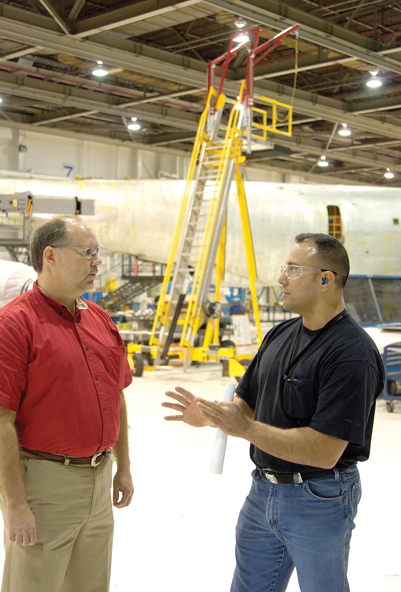 An extended ladder system, jokingly called “the diving board,” sits in the background while 564th Aircraft Maintenance Squadron mechanic Nicholas Deilami, right, and safety inspector Mike Ward chat. The system allows workers to be harnessed while working on aircraft. (Air Force photo by Margo Wright)