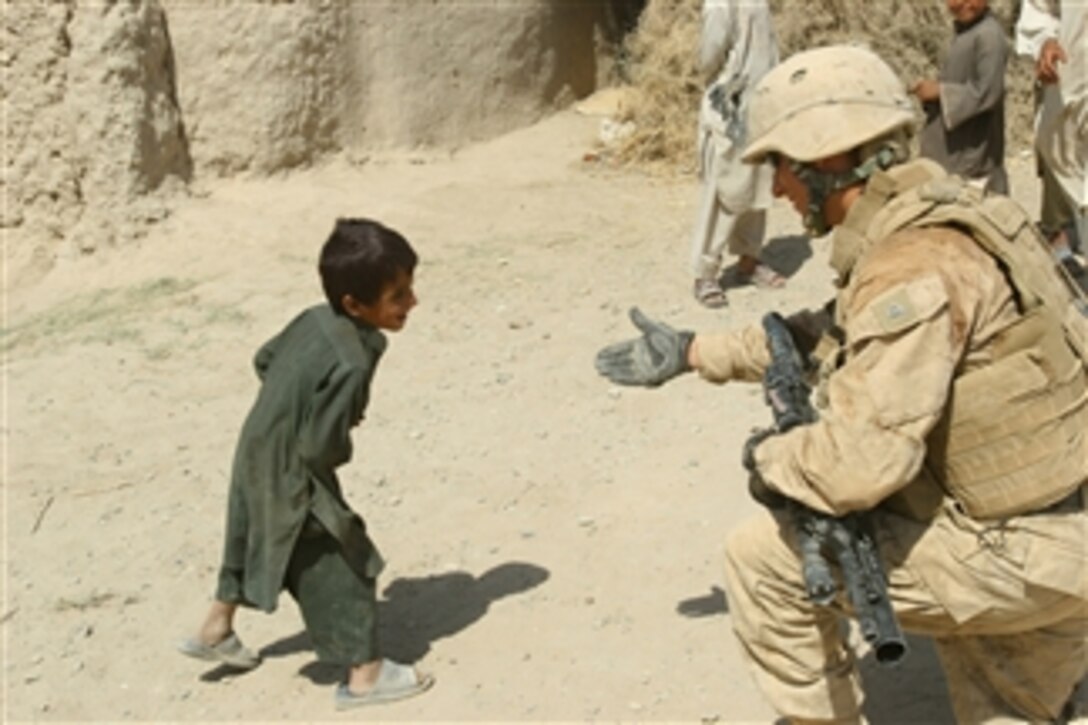 A U.S. Marine attached to Mine-Resistant, Ambush-Protected Company, Regimental Combat Team 3 holds out his hand to an Afghan boy in Helmand province, Afghanistan, on Sept. 19, 2009.  The Marines are conducting a convoy to forward operating bases and combat outposts to deliver exchange items, mail and services.  Regimental Combat Team 3 is deployed to Afghanistan to train and mentor Afghan National Security Forces and help fight counterinsurgency at the request of the Afghan government.  