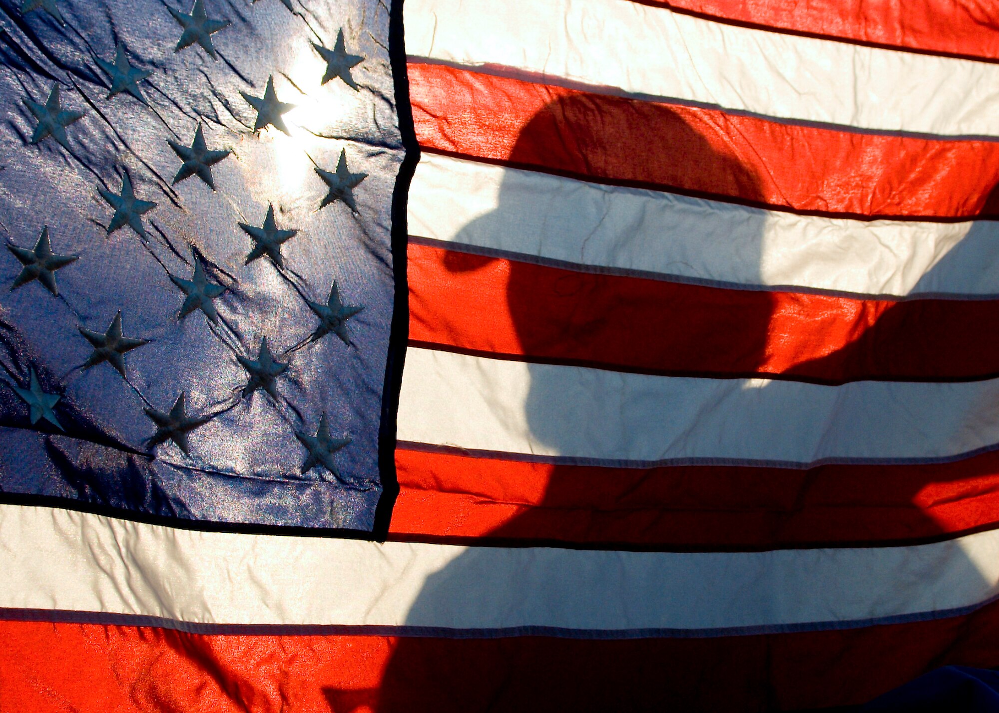 Joseph Johnson, a former prisoner of war, creates a silhoutte on the American Flag, as he stands at the finish line of Edwards POW/MIA Day ruck march Sept. 17. Team Edwards commemorated POW/MIA Day Sept. 17 and 18 with a ruck march, luncheon and a retreat ceremony. (Air Force photo/ Mike Cassidy)