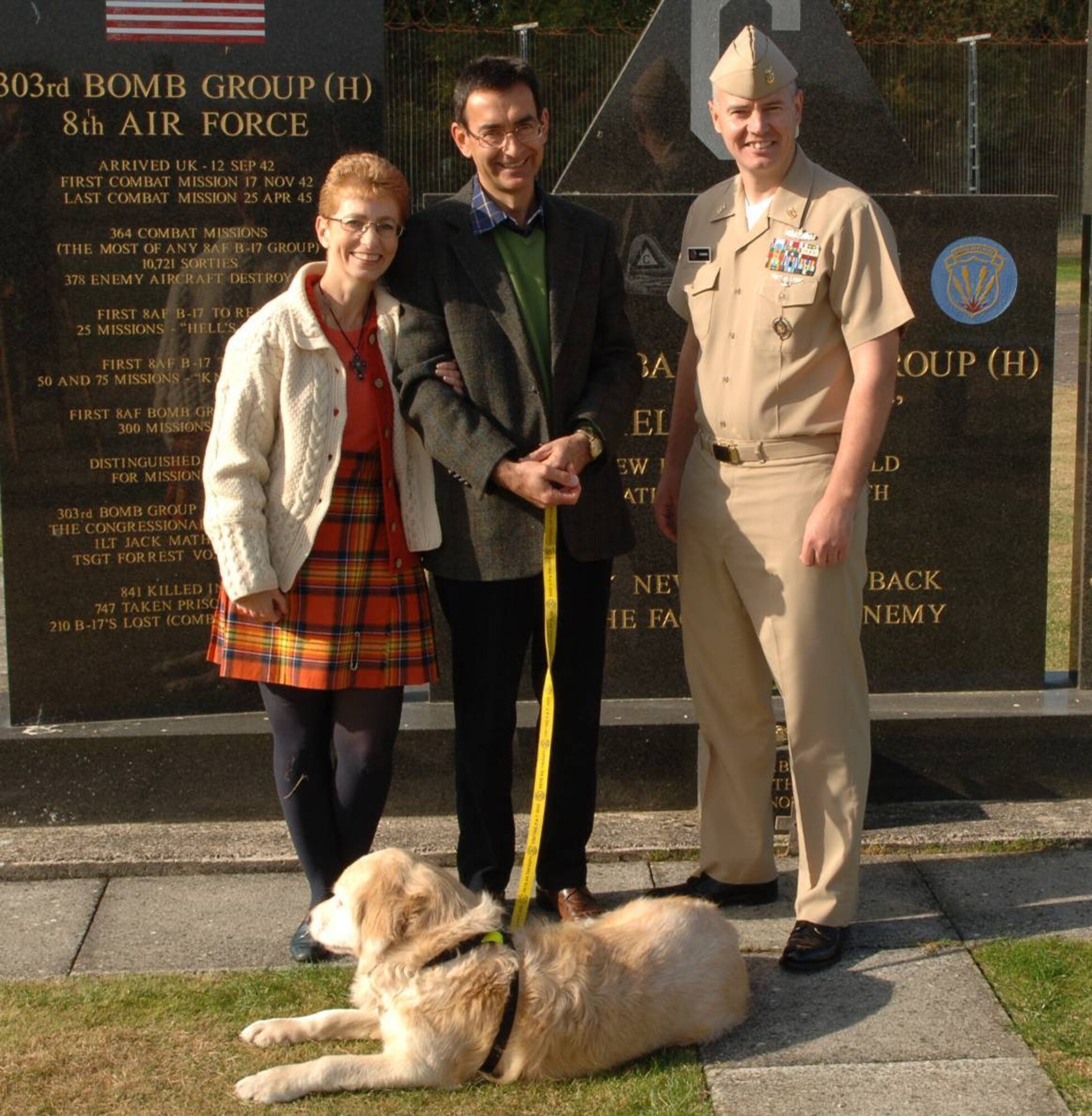 Ms. Louise Smedley-Hampson, her husband John, and retired Patient Assistance Dog "Teddy" are welcomed at the 303rd Bomb Group (Heavy) Memorial by JIOCEUR Analytic Center Senior Enlisted Leader, Navy Master Chief John C. Frakes.  Ms. Smedley Hampson visited RAF Molesworth, England on September 25th to commemorate the life of Staff Sgt. Joseph G. "Zip" Zsampar, U.S. Army Air Corps to whom her mother was engaged before his B-17 Flying Fortress was shot down in May 1943. (U.S. Air Force Photo by Staff Sgt. Javier Cruz)