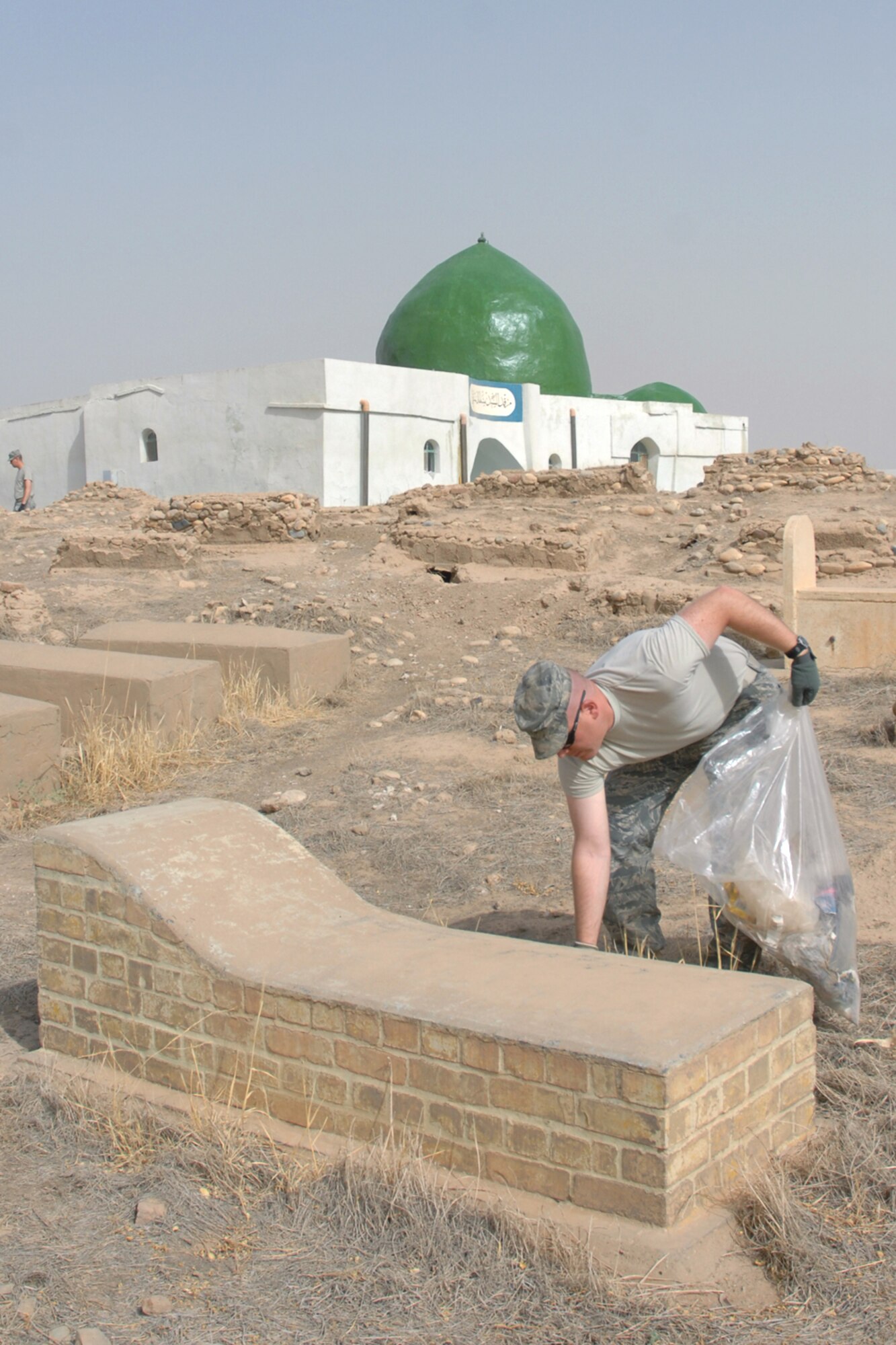 KIRKUK REGIONAL AIR BASE, Iraq – Tech. Sgt. John Wulff, 506th Expeditionary Security Forces Squadron, picks up garbage near a gravesite while volunteering to clean up the Sultan Saqi cemetery here Sept. 18.  Sixteen volunteer Airmen from the 506th ESFS took part in the cleanup in preparation for the end of the month of Ramadan.  Sergeant Wulff is deployed here from the 446nd SFS, McChord Air Force Base, Wash. (U.S. Air Force photo/Staff Sgt. Daniel Martinez)  
