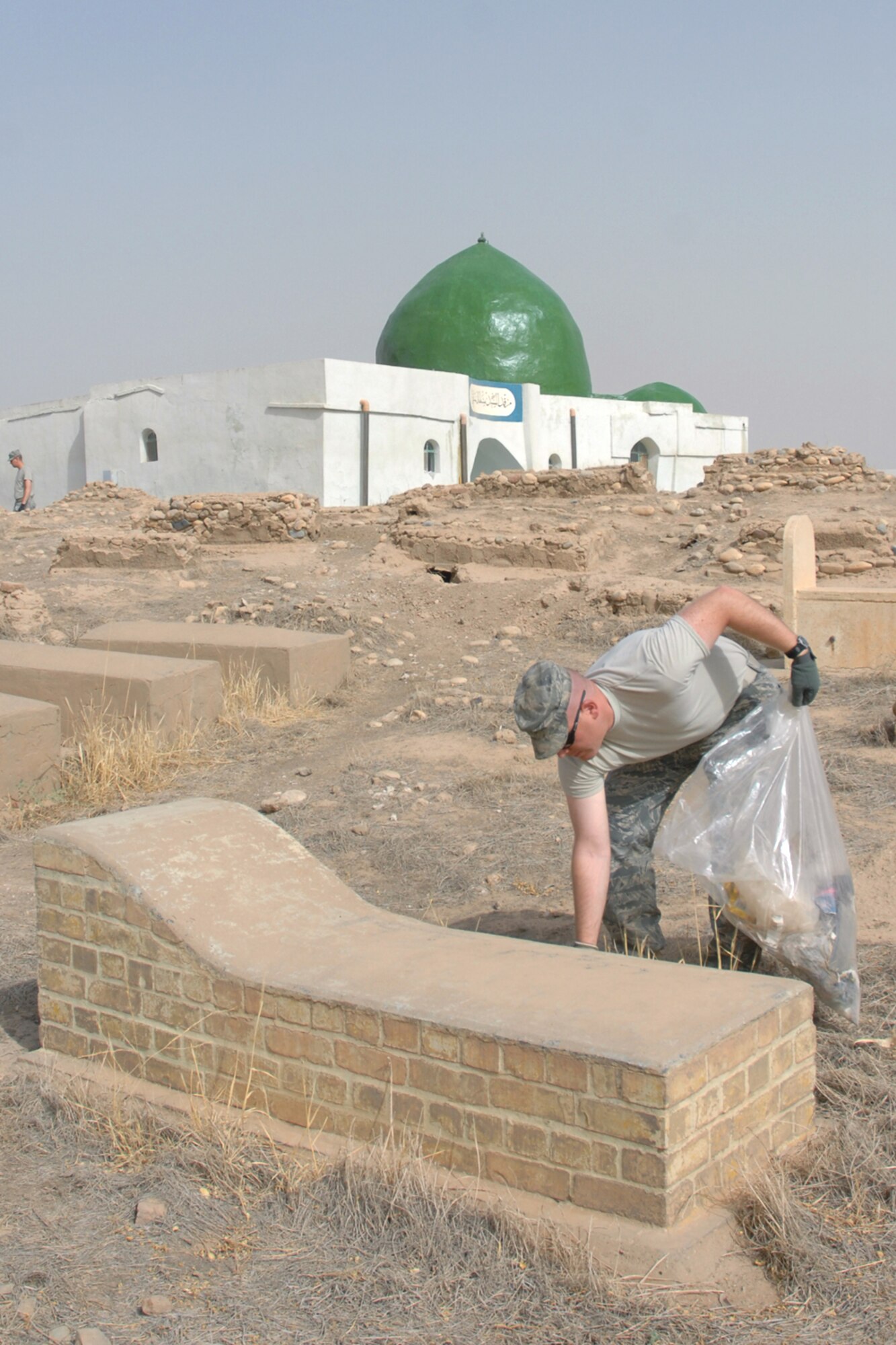 KIRKUK REGIONAL AIR BASE, Iraq – Tech. Sgt. John Wulff, 506th Expeditionary Security Forces Squadron, picks up garbage near a gravesite while volunteering to clean up the Sultan Saqi cemetery here Sept. 18.  Sixteen volunteer Airmen from the 506th ESFS took part in the cleanup in preparation for the end of the month of Ramadan.  Sergeant Wulff is deployed here from the 446nd SFS, McChord Air Force Base, Wash. (U.S. Air Force photo/Staff Sgt. Daniel Martinez)  