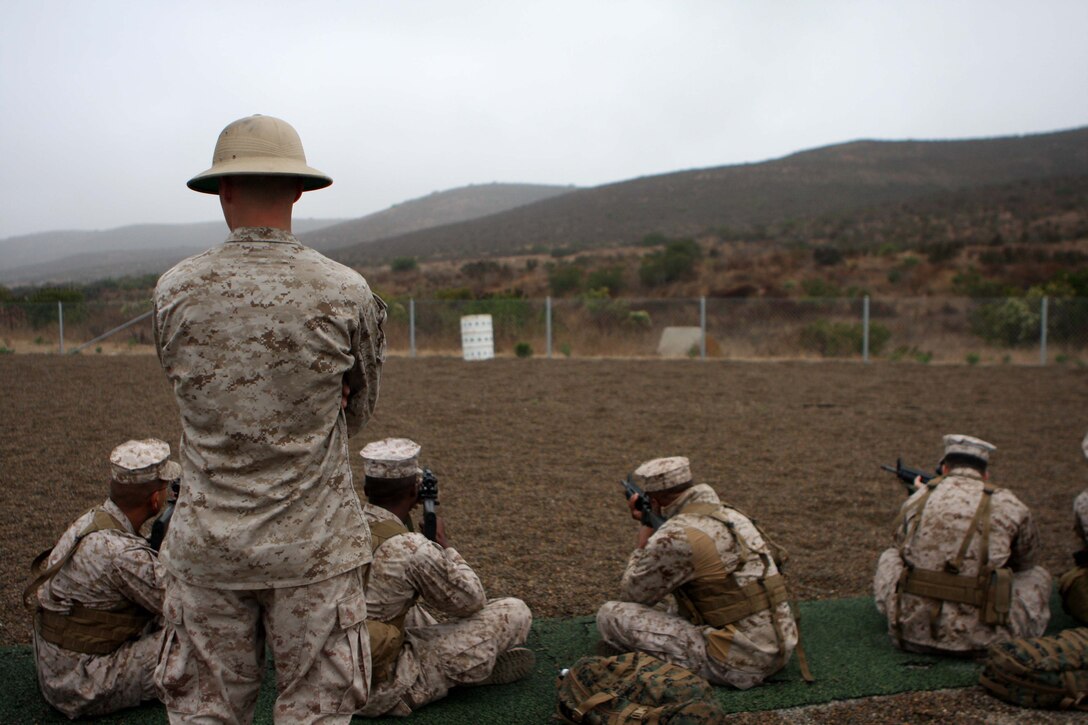 Lance Cpl. Justin Jennings, a combat marksmanship trainer at the Carlos Hathcock Range here, observes his students as they practice the sitting position for their upcoming rifle qualification, Oct. 15.  Instructors like Jennings teach Marines the fundamentals of Corps marksmanship like sighting in and breathing techniques.
