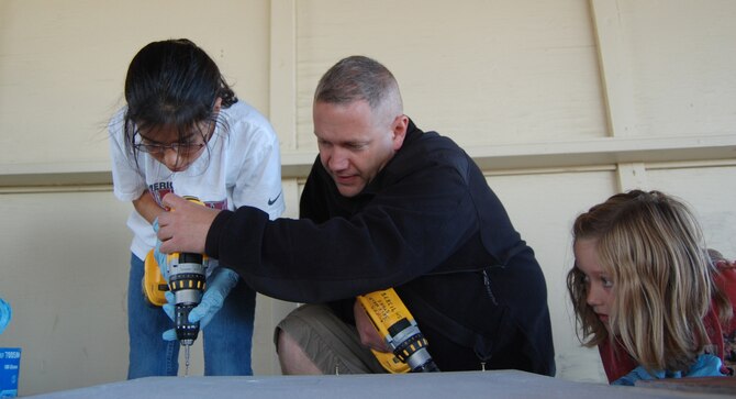 Alexis Crow, 10, carefully lines up her drill bit in the screw head before pulling the trigger on the screw gun while Master Sgt. Jason Broach lends some extra guidance. Rylee Broach, 9, looks on. The girls are Scouts with Malmstrom's Troop 3135 and they were working on a National Public Lands Day project to build bat houses for Pow Wow Park Sept. 26. (U.S. Air Force photo/Valerie Mullett)