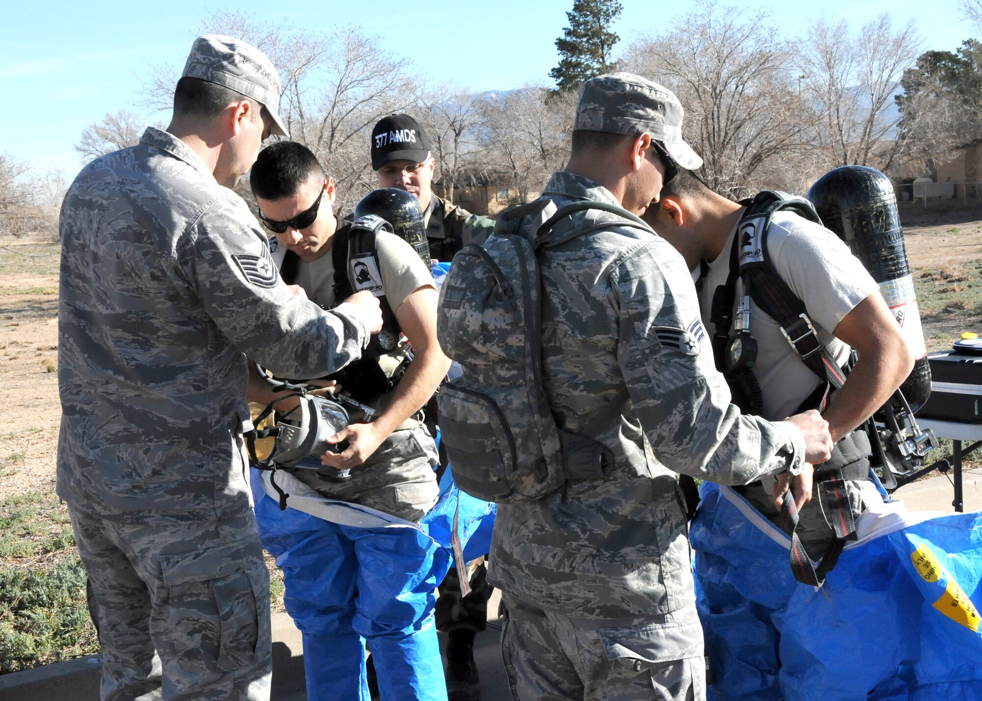Tech. Sgt. Joe Mulgado, left, and Senior Airman Gene Davila assist Senior Airmen Omar Gutierrez-Moreno, left, and John Gonzalez, all from the 377th Bioengineering Flight, into their exercise hazmat suits during an exercise held behind the Commissary, March 17.

U.S. Air Force Photo by Dennis Carlson