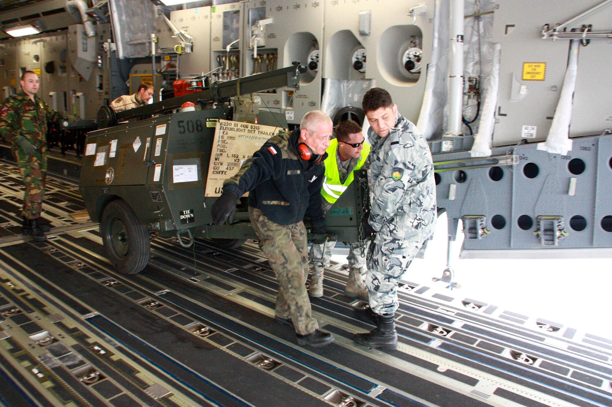Airmen from the multinational Heavy Airlift Wing move a floodlight set trailer in preparation for shipment to units in Afghanistan, March 30. The HAW moved more than 2.1 million pounds of War Reserve Material essential to surge operations supporting the International Security Assistance Force in Afghanistan. The HAW, based at Pápa Air Base, Hungary, operates three C-17 Globemaster III aircraft independently of NATO's military command and is comprised of 12 nations that activated the unit, July 27, 2009. (Photo by Finnish Capt. Juha Miettinen, HAW)