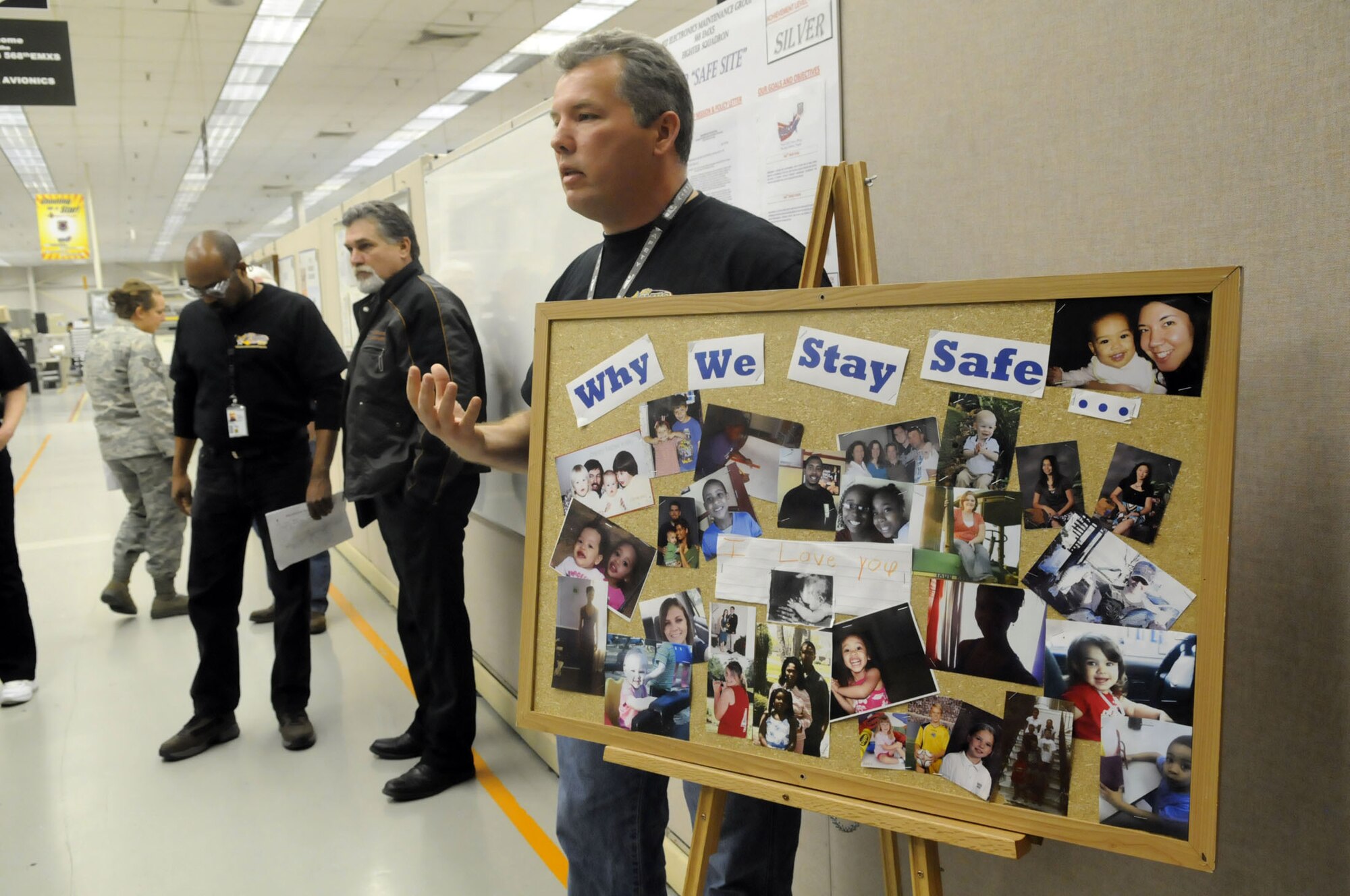 Joe Martin shows off a bulletin board to evaluation members showing photographs of worker's loved ones to show the importance of VPP. U. S. Air Force photo by Sue Sapp