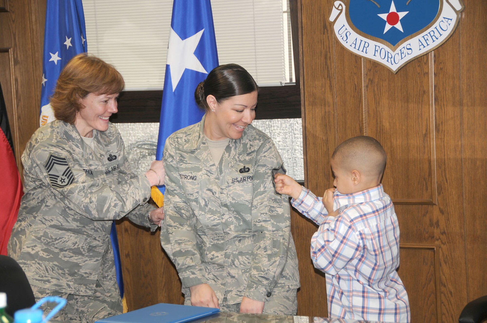 Master Sgt. Amanda Armstrong receives help tacking on her master sergeant stripes from her son Esteban, and from Chief Master Sgt. Karen Thomas, during her promotion ceremony Mar. 31. Master Sgt. Armstrong’s husband, who is deployed, watched via Video Teleconference. Chief Thomas is the U.S. Air Forces Europe command services functional manager and Master Sgt. Armstrong is the 17th Air Force NCO in charge of services readiness. (U.S. Air Force photo by Staff Sgt. Stefanie Torres)