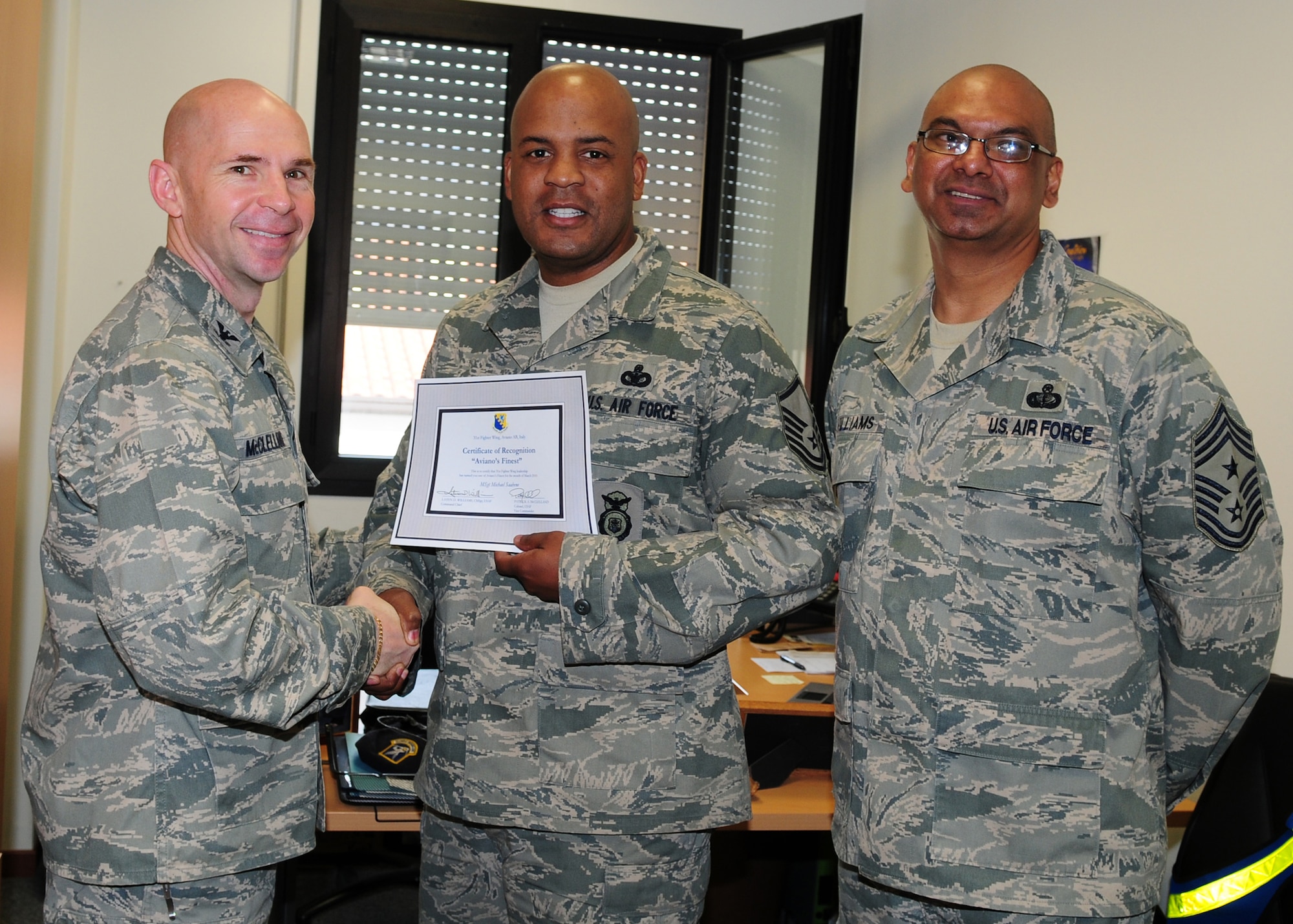 Col. Patrick A. McClelland, 31st Fighter Wing vice commander, congratulates Master Sgt. Michael Saahene, 31st Security Forces Squadron logistics superintendent on his selection as one of Aviano's Finest as Chief Master Sgt. Laten Williams, 31st FW command chief, looks on. (U.S. Air Force photo/ Senior Airman Taylor Marr)
