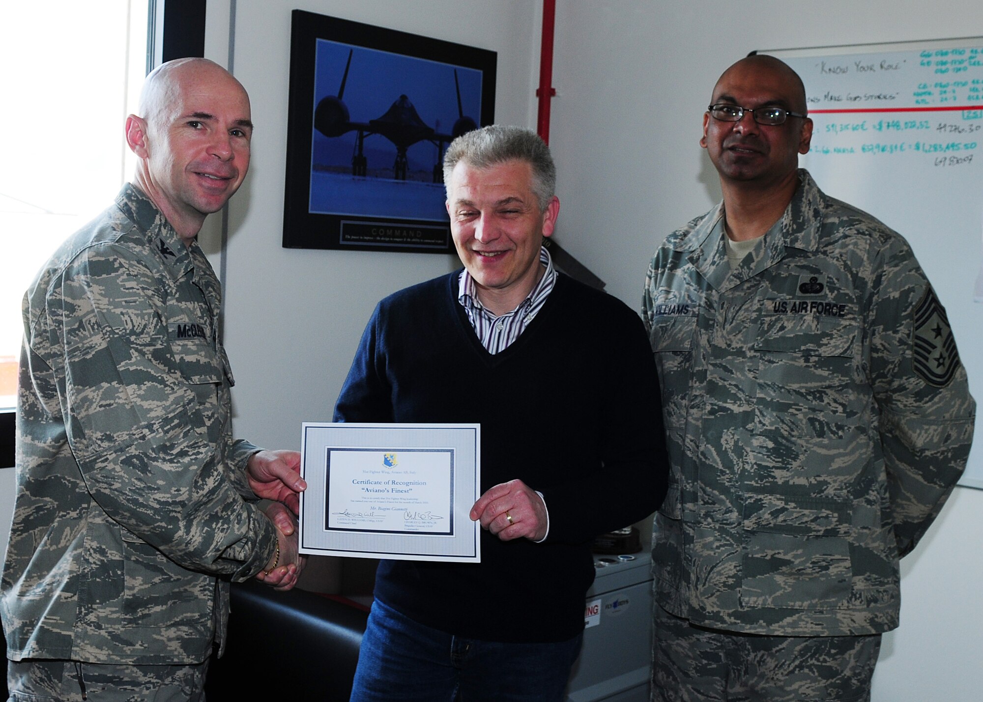 Col. Patrick A. McClelland, 31st Fighter Wing vice commander, congratulates Mr. Biagino Giannotti,, 31st Security Forces Squadron interpreter, on his selection as one of Aviano's Finest as Chief Master Sgt. Laten Williams, 31st FW command chief, looks on. (U.S. Air Force photo/ Senior Airman Taylor Marr)
