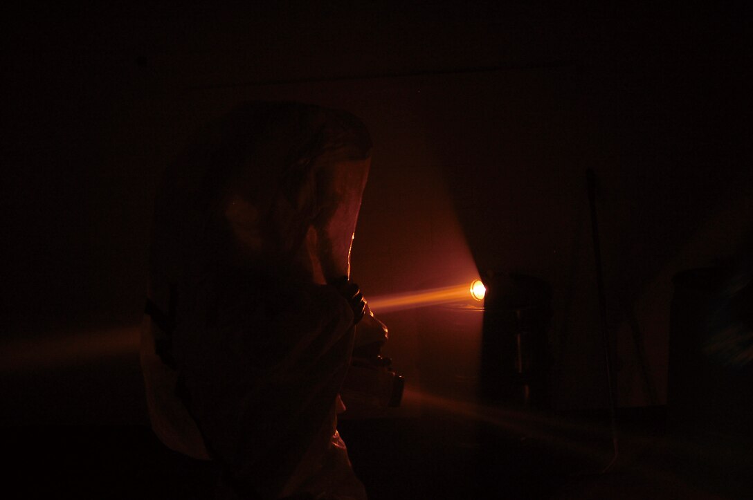A Marine in a protective suit uses a flashlight inside a simulated contaminated building to try to locate suspected chemical hazards during a week long Hazardous Waste Operations and Emergency Response Course aboard Camp Foster April 2.