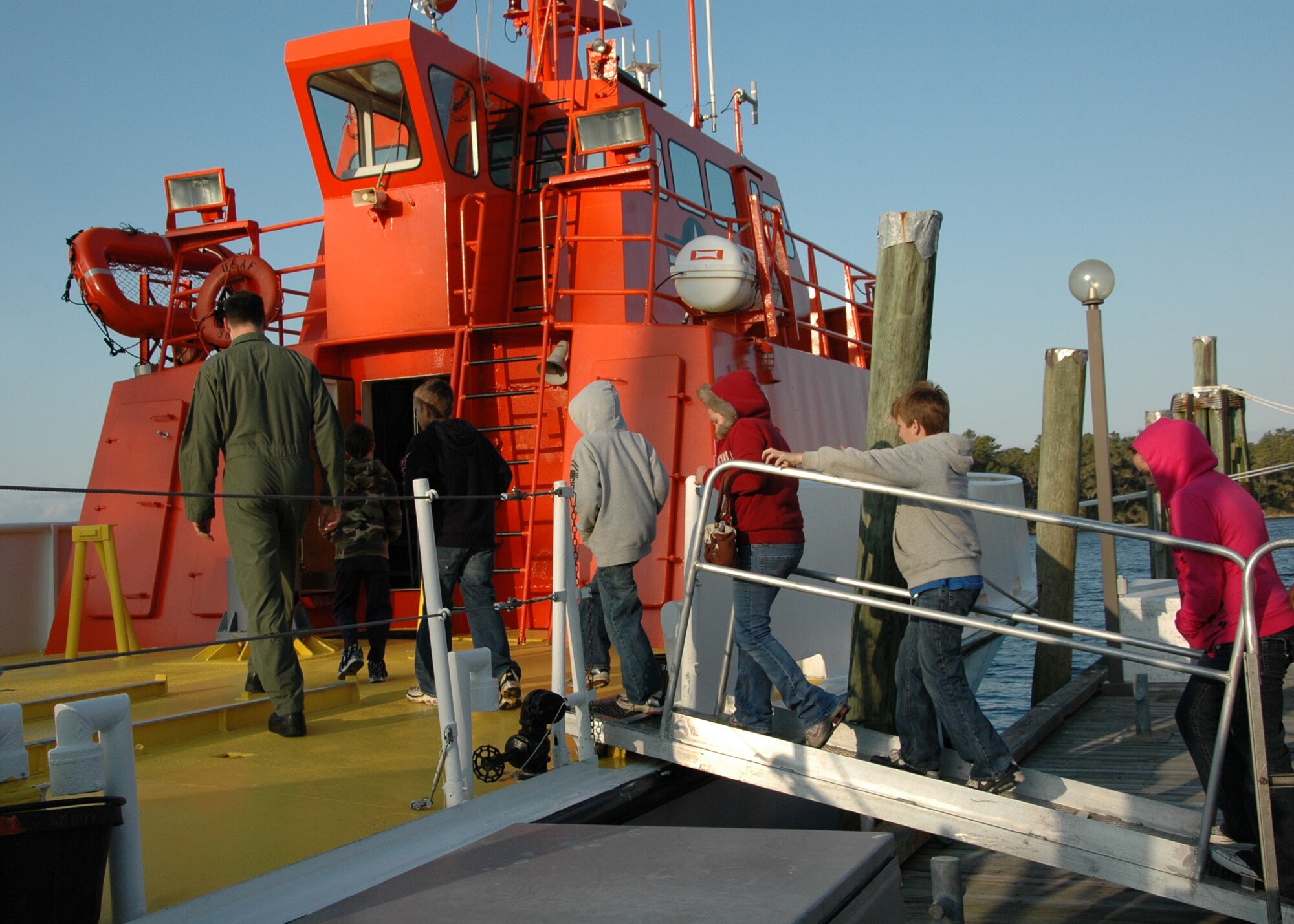 Maj. Joseph Michaelson, 53rd Weapons Evaluations Group E-9 pilot, leads children from the Taunton Family Children’s Home onto an 82nd Aerial Targets Squadron’s 120-foot drone recovery vessel. The group toured Tyndall Air Force Base, Fla., March 26 during their spring break to see the Air Force in action. (U.S. Air Force photo/ Ashley M. Wright)