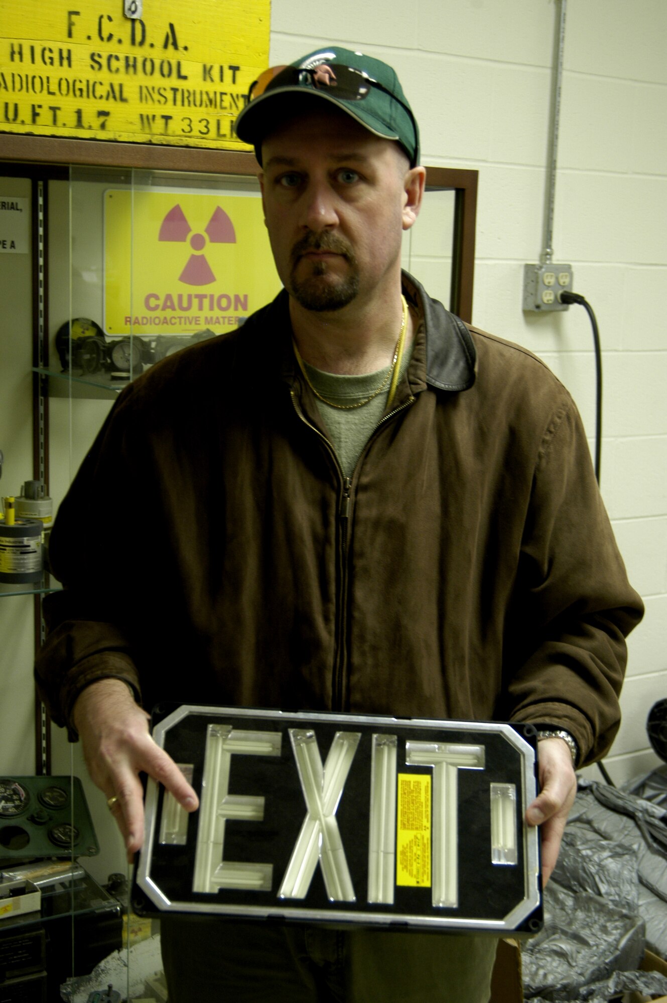 Air Force Radioactive Recycling And Disposal (AFRRAD) Chief of Radiation Management Branch Brian Harcek holds an old self lighting exit sign with tritium which was used to light the sign.  The outer casing and plastic are removed and sent to the base recycling center.   The rest of the sign is sent to a vendor in Las Vegas to recover the tritium. (U.S. Air Force by Ted Theopolos)
