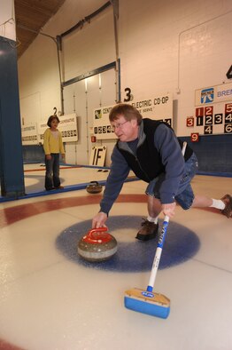 MINOT, N.D. -- Ron Anderson, Minot Curling Club league chairman, shows Mia Arellano, daughter of Laurie Arellano, 5th Bomb Wing chief of public affairs, how to throw the stone during a curling lesson March 26 at the Minot Curling Club. The Minot Curling Club is open November through March and provides lessons and competition opportunities for Minot Airmen and family members of all skill levels. (U.S. Air Force photo by Staff Sgt. Stacy Moless)