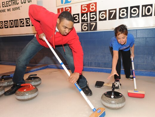 MINOT, N.D. -- Airman 1st Class Aaron Wainwright, 5th Bomb Wing photographer, and Allie Arellano, daughter of Laurie Arellano, 5th Bomb Wing chief of public affairs, try out sweeping and throwing stones during a curling lesson March 26 at the Minot Curling Club.  The Minot Curling Club is open November through March and provides lessons and competition opportunities for Minot Airmen and family members of all skill levels. (U.S. Air Force photo by Staff Sgt. Stacy Moless)