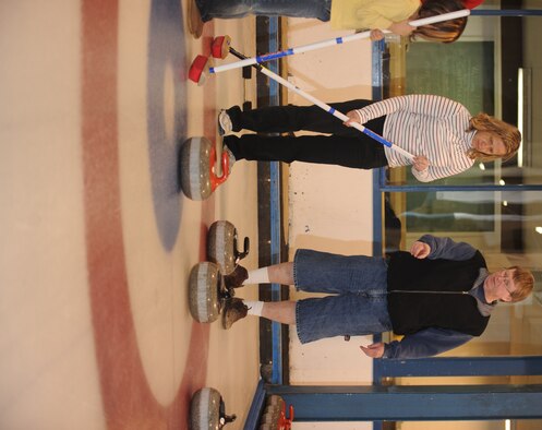 MINOT, N.D. -- Ron Anderson, Minot Curling Club league chairman, shows Laurie Arellano, 5th Bomb Wing chief of public affairs, and her daughter Mia, how to sweep during a curling lesson March 26 at the Minot Curling Club.  The Minot Curling Club is open November through March, and provides lessons and competition opportunities for Minot Airmen and family members of all skill levels. (U.S. Air Force photo by Staff Sgt. Stacy Moless)