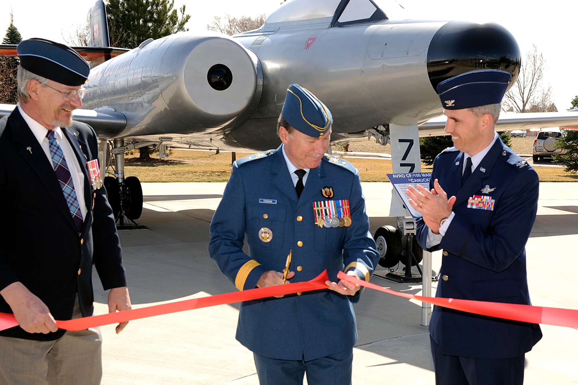 PETERSON AIR FORCE BASE Colo. -- Standing in front of the CF-100 Mark 5C “Canuck” Canadian aircraft in Peterson Air and Space Museum Park, Brig. Gen. Robert Chekan, North American Aerospace Defense Command deputy director of plans, policy and strategy, cuts the ribbon April 1 in a rededication ceremony of two Canadian aircraft. Joining him are retired Master Warrant Officer Darrell Leavitt, (left) and Col. Stephen N. Whiting, 21st Space Wing commander, (right). The rededication of the CF-101B “Voodoo,” and the CF-100 Mark 5C “Canuck,” marked the 86th anniversary of the Royal Canadian Air Force. The “Voodoo” first flew in 1957 and is a long-range all-weather interceptor. It has been in the air park since 1984. The “Canuck” is an all-weather jet fighter, equipped with radar jammers, and flew from 1952 to 1981. It was gifted to the air park in 1976. Approximately 140 Canadian forces personnel work on Peterson Air Force Base. (U.S. Air Force photo/Larry Hulst)