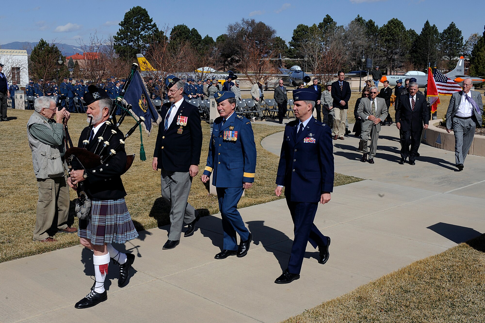 PETERSON AIR FORCE BASE, Colo. -- Pipe Major Sam Swancutt leads an official party, including (from left) retired Canadian Forces Master Warrant Officer Darrell Leavitt, Brig. Gen. Robert Chekan, North American Aerospace Defense Command deputy director of plans, policy and strategy, and Col. Stephen N. Whiting, 21st Space Wing commander, to a ribbon cutting at the Peterson Air and Space Museum Park April 1. The group was marking the rededication of two Canadian aircraft. The aircraft, a CF-101 B “Voodoo,” and the CF-100 Mark 5C “Canuck,” were rededicated to mark the 86th anniversary of the Royal Canadian Air Force. The “Voodoo” first flew in 1957 and is a long range all-weather interceptor. It has been in the air park since 1984. The “Canuck” is an all-weather jet fighter, equipped with radar jammers, and flew from 1952 to 1981. It was gifted to the air park in 1976. Approximately 140 Canadian personnel work on Peterson Air Force Base. (U.S. Air Force photo/Larry Hulst)