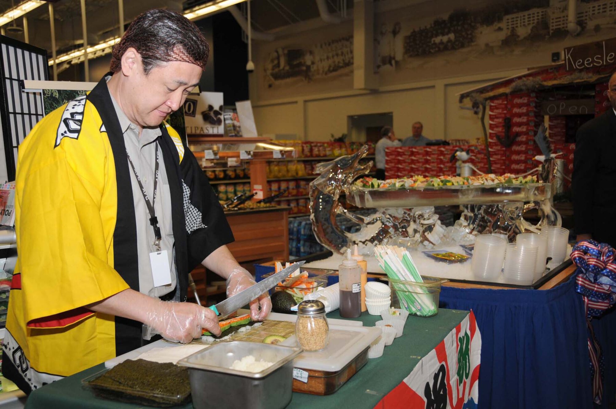 Tye Wada prepares sushi samples kept chilled in a dragon ice sculpture on opening day at the commissary.  In addition to the commissary and base ex-change, the $60 million shopping complex includes a pharmacy, food court, optical shop, GNC, a variety of concessionaires and beauty, nail and barber shops.  (U.S. Air Force photo by Kemberly Groue)