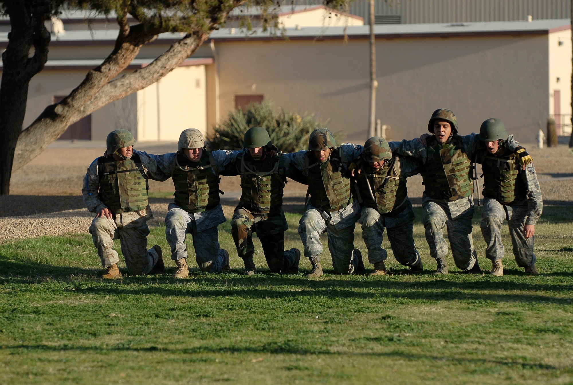 Participants of a military combative training course form a line and perform lunges across a field in unison near the Silver Wings pool at Luke Air Force Base, Ariz., April 5. This exercise helps construct team building skills as well as physical fitness in combative attire.  (U.S. Air Force photo by Airman 1st Class Ronifel Yasay)