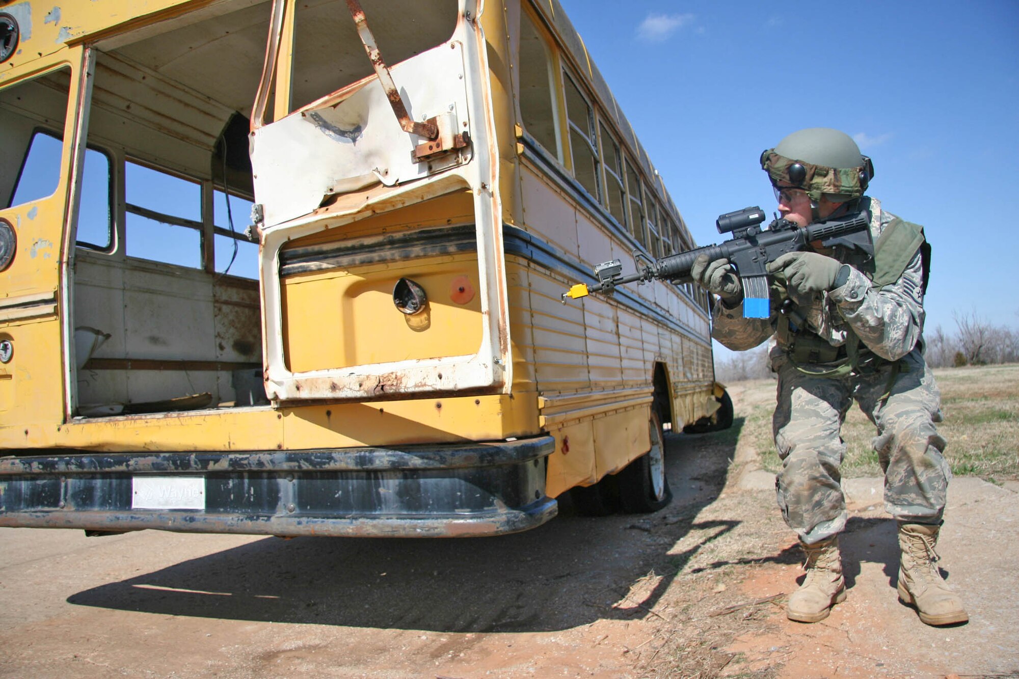 Staff Sgt. Jarod Williams with the 3rd Combat Communications Group peers around a school bus used for cover from enemy fire during a combat training exercise at Tinker’s Glenwood Training Area March 17. Airmen from the 3rd Herd, and four other communications groups from Air Force Space Command, will participate in a combat competition here April 16-19.