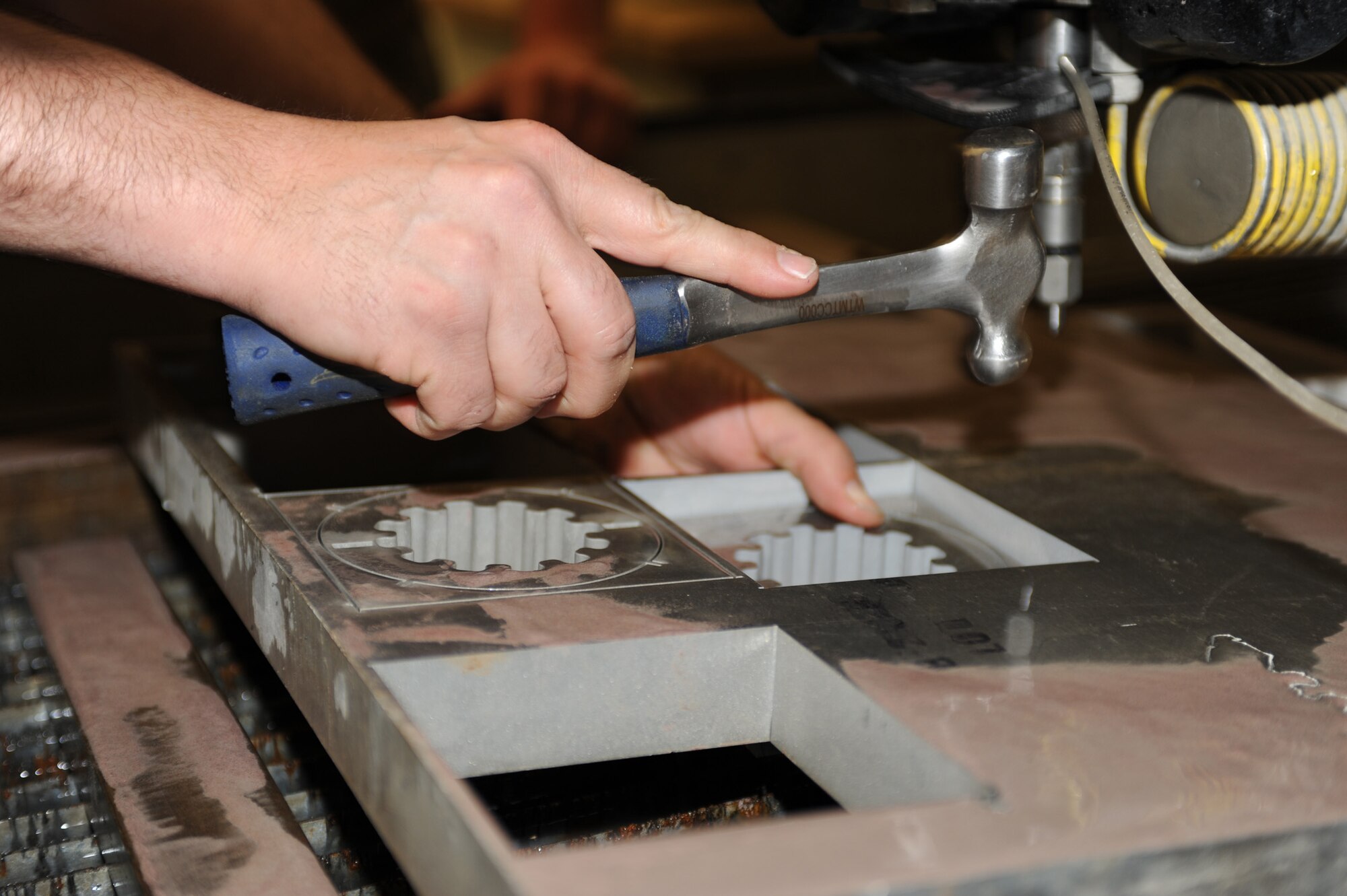 WHITEMAN AIR FORCE BASE,Mo.- Master Sgt. Carl Schilli, 131st Maintenance Squadron metals technician, taps out a fresh cut nozzle after being carved out by a water jet computer numerical control system from a large slab of metal, April 6, 2010. Metals technology designs and fabricates multiple pieces for the Team Whiteman mission, for everyday use in every career field. (U.S. Air Force photo/ Airman 1st Class Carlin Leslie) (Released)