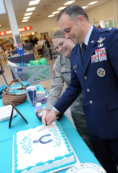 RAF MILDENHALL, England -- Tech. Sgt. Amy Underwood, 100th Operations Support Squadron (left), and Col. Michael Winters, 100th Air Refueling Wing vice commander, perform a traditional cake cutting to open a Sexual Assault Awareness Month information booth at the Base Exchange here April 7. This event was hosted by the Sexual Assault Prevention and Response Office to highlight the April awareness campaign.  (U.S. Air Force photo/Staff Sgt. Thomas Trower)