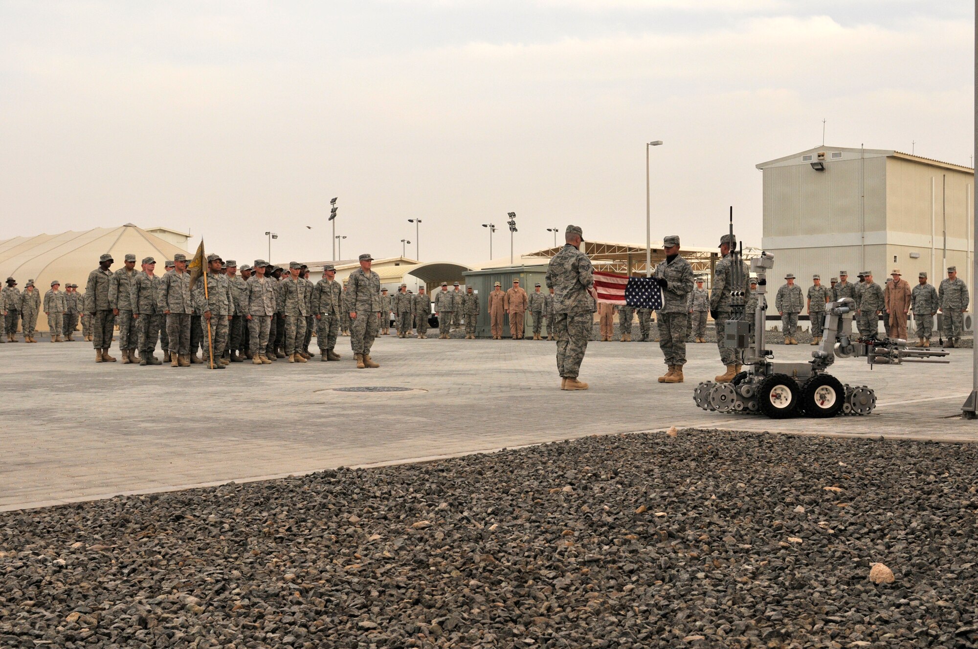 Lt. Col. William Kale III, 380th Expeditionary Civil Engineering Squadron Commander, takes the lead of this CE formation April 9 at an undisclosed location in Southwest Asia, but when an Air Force explosive ordinance disposal technician heads downrange, the robot goes first. Robotic systems like this one to the left of the flag have saved numerous lives by helping to eliminate the threat of improvised explosive devices encountered in deployed locations. The 380th Air Expeditionary Wing brings together active duty, reserve and Air National Guard Airmen joined with civilian patriots and DoD contractors to carry out its diverse mission of all-weather high-altitude ISR, airborne command and control and air refueling with a "One Team, One Fight" attitude. (U.S. Air Force Photo/Capt. Cathleen Snow/Released)