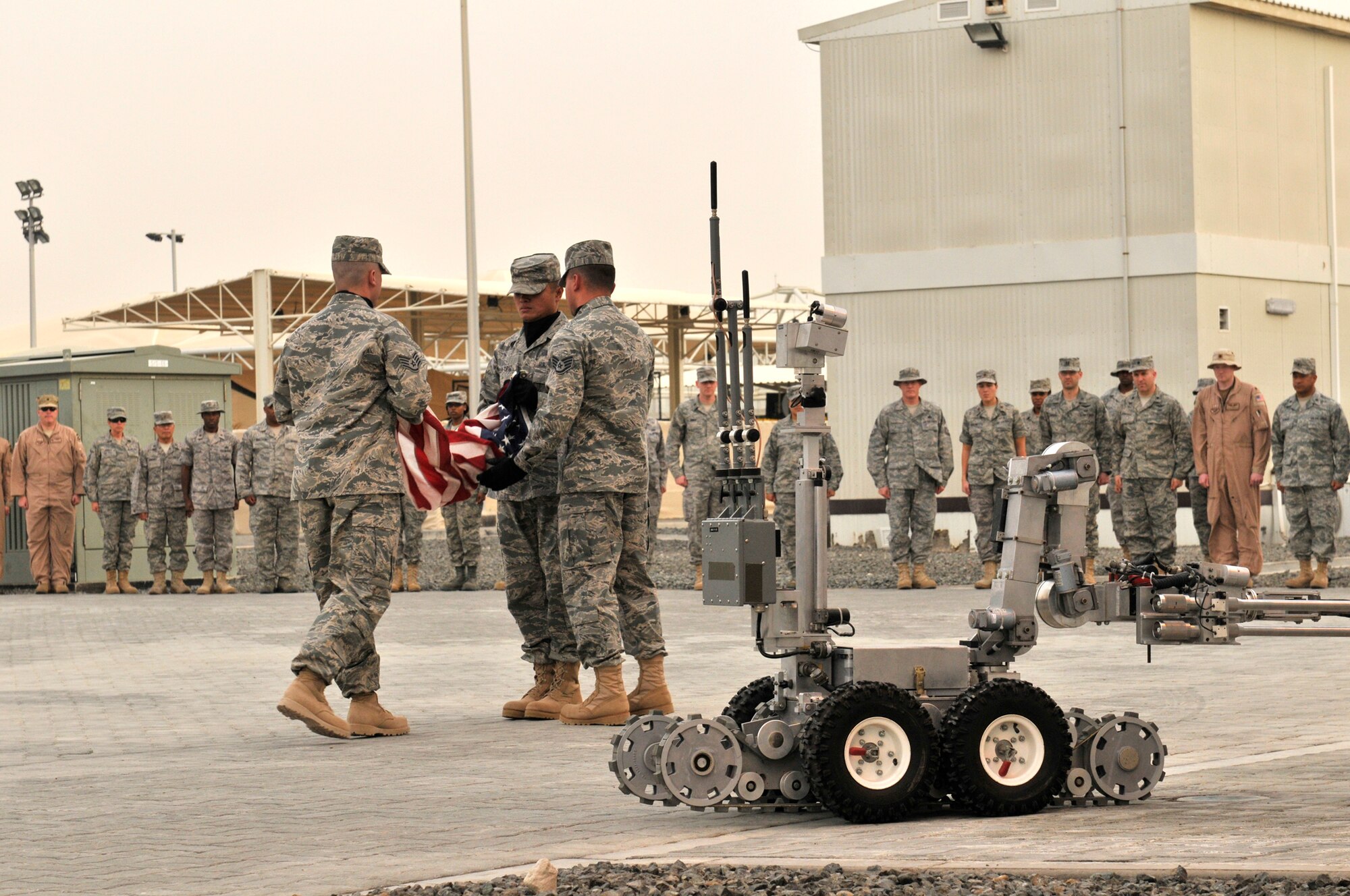 Airmen from the 380th Expeditionary Civil Engineering Squadron, at an undisclosed location in Southwest Asia, take the lead in folding the American flag for this CE retreat formation April 9, but when an Air Force explosive ordinance disposal technician heads downrange, the robot goes first. Robotic systems like this one to the right of the flag have saved numerous lives by helping to eliminate the threat of improvised explosive devices which troops encounter in Afghanistan. The 380th Air Expeditionary Wing brings together active duty, reserve and Air National Guard Airmen joined with civilian patriots and DoD contractors to carry out its diverse mission of all-weather high-altitude ISR, airborne command and control and air refueling with a "One Team, One Fight" attitude. (U.S. Air Force Photo/Capt. Cathleen Snow/Released)