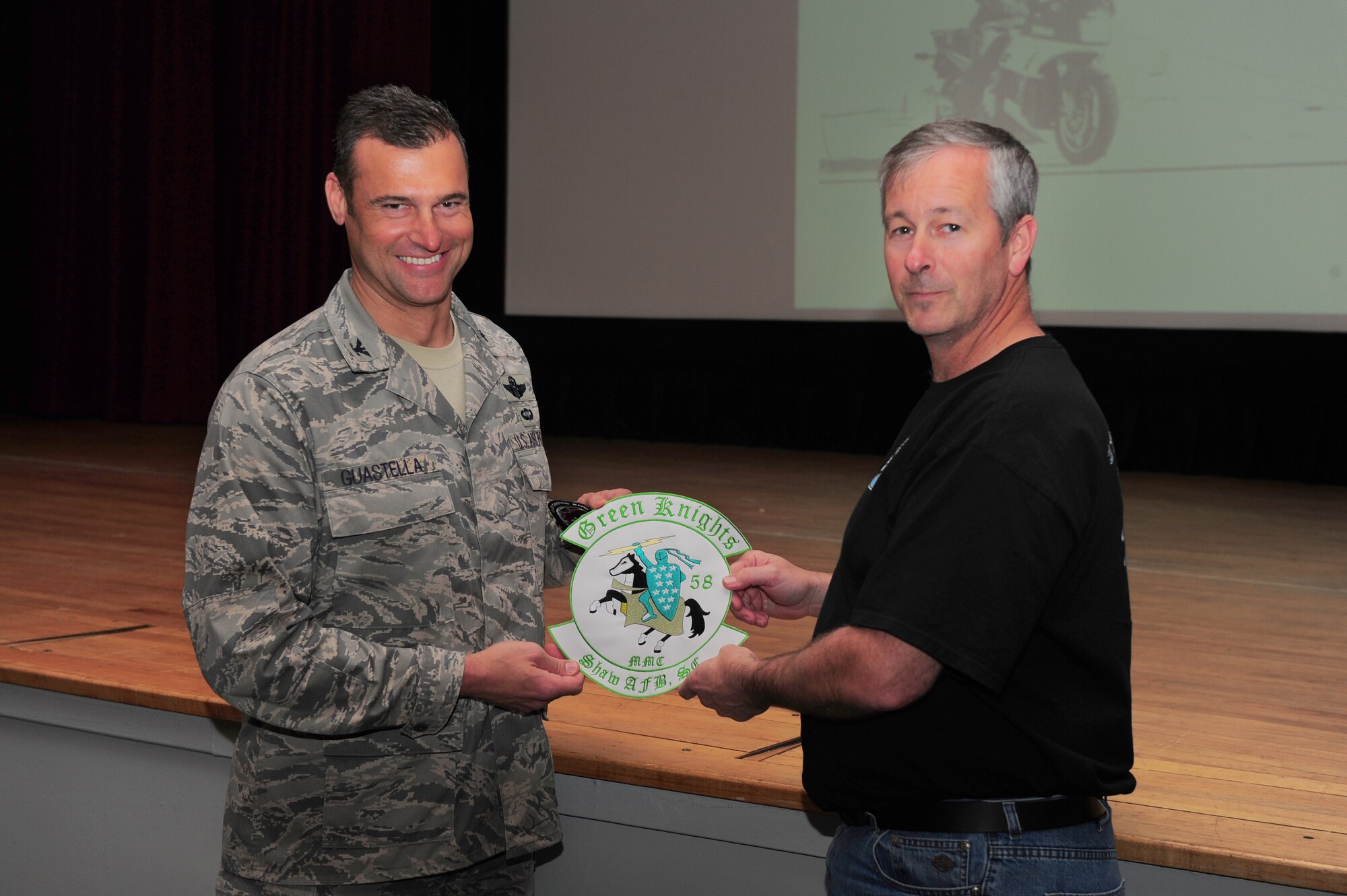 SHAW AIR FORCE BASE, S.C. -- Terry Grimm, retired Air Force senior master sergeant, inducts Col. Joe Guastella, 20th Fighter Wing commander, into the Green Knights motorcycle club as an honorary member. Grimm presents Colonel Guastella with a jacket patch at the base theater here April 8. The Green Knights are a military affiliated motorcycle club with 80 chapters in 13 countries. Their focus is to improve each individual's motorcycle riding experience and to educate them on safety, rider skills, community and family enhancement. (U.S. Air Force photo by Senior Airman David Minor)